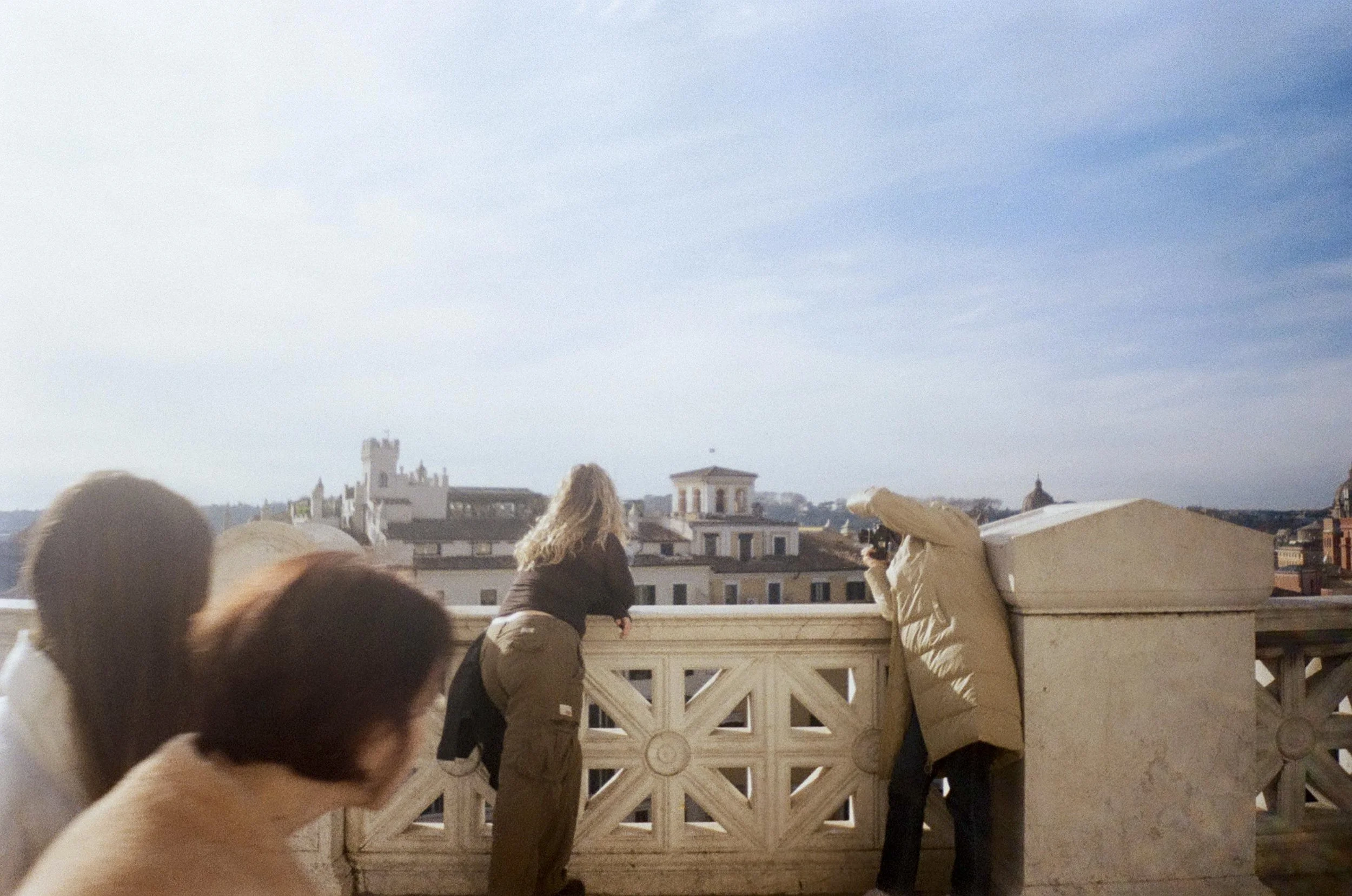 Woman taking photo of another woman on top of a castle in Rome as onlookers peek in.