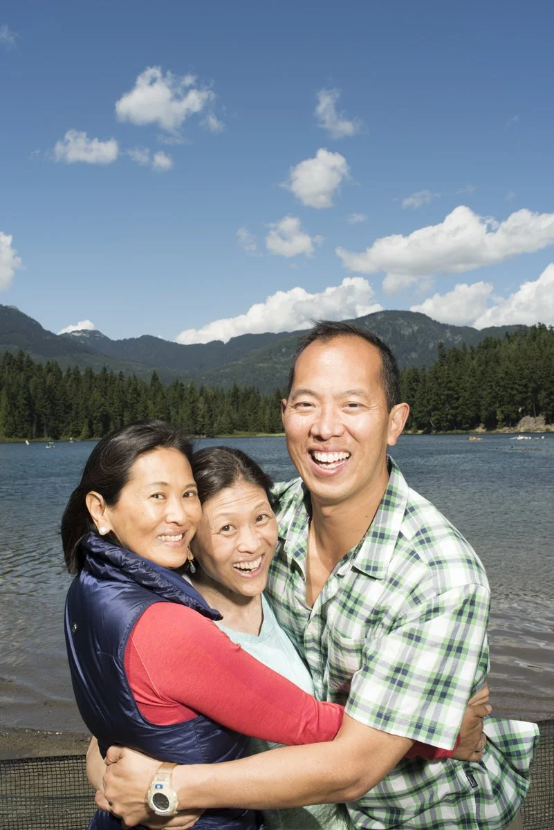 Adult siblings hugging and laughing by a lake in Whistler during a family reunion