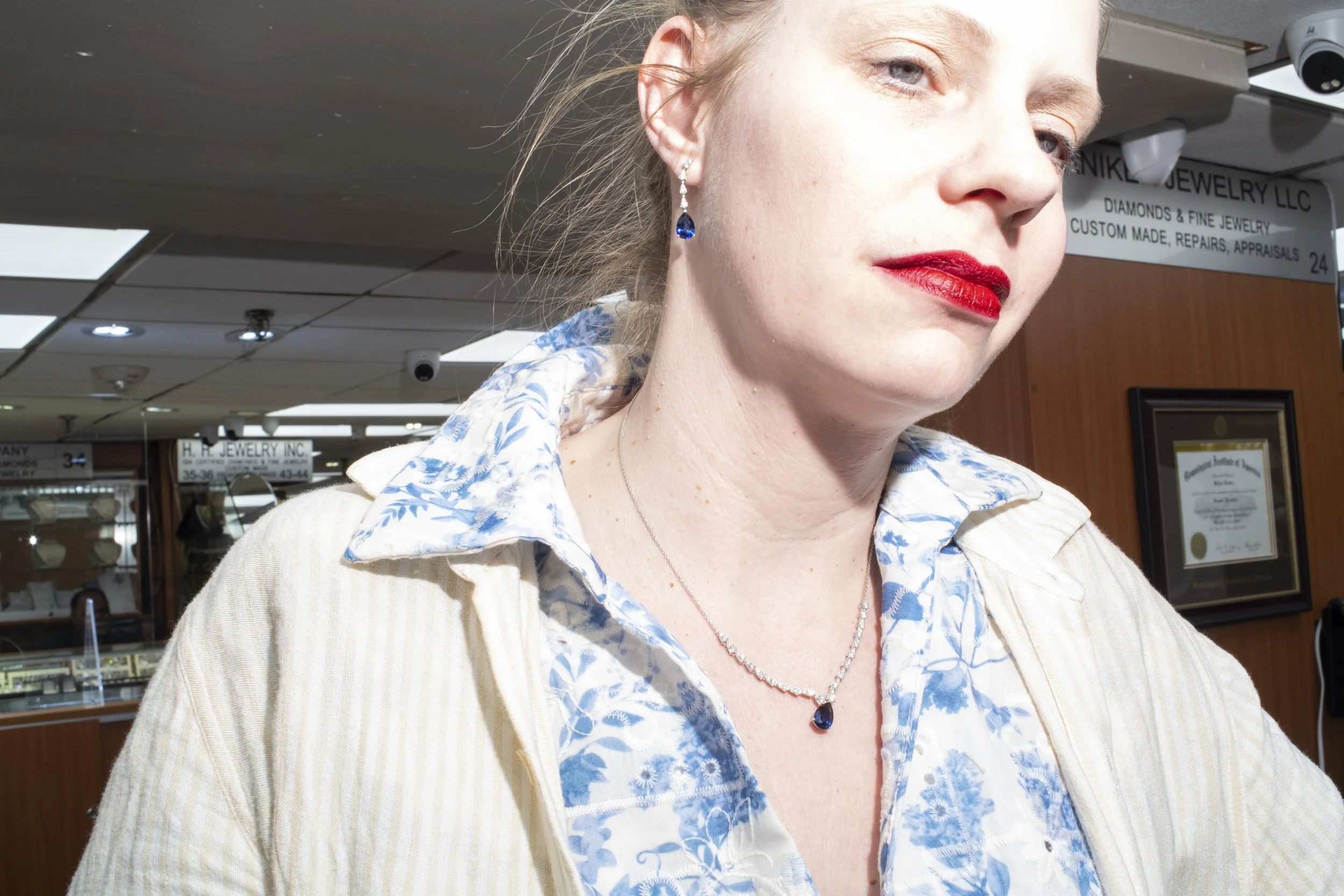Mid 30's woman with pale skin wears deep blue sapphires and an open collar shirt.