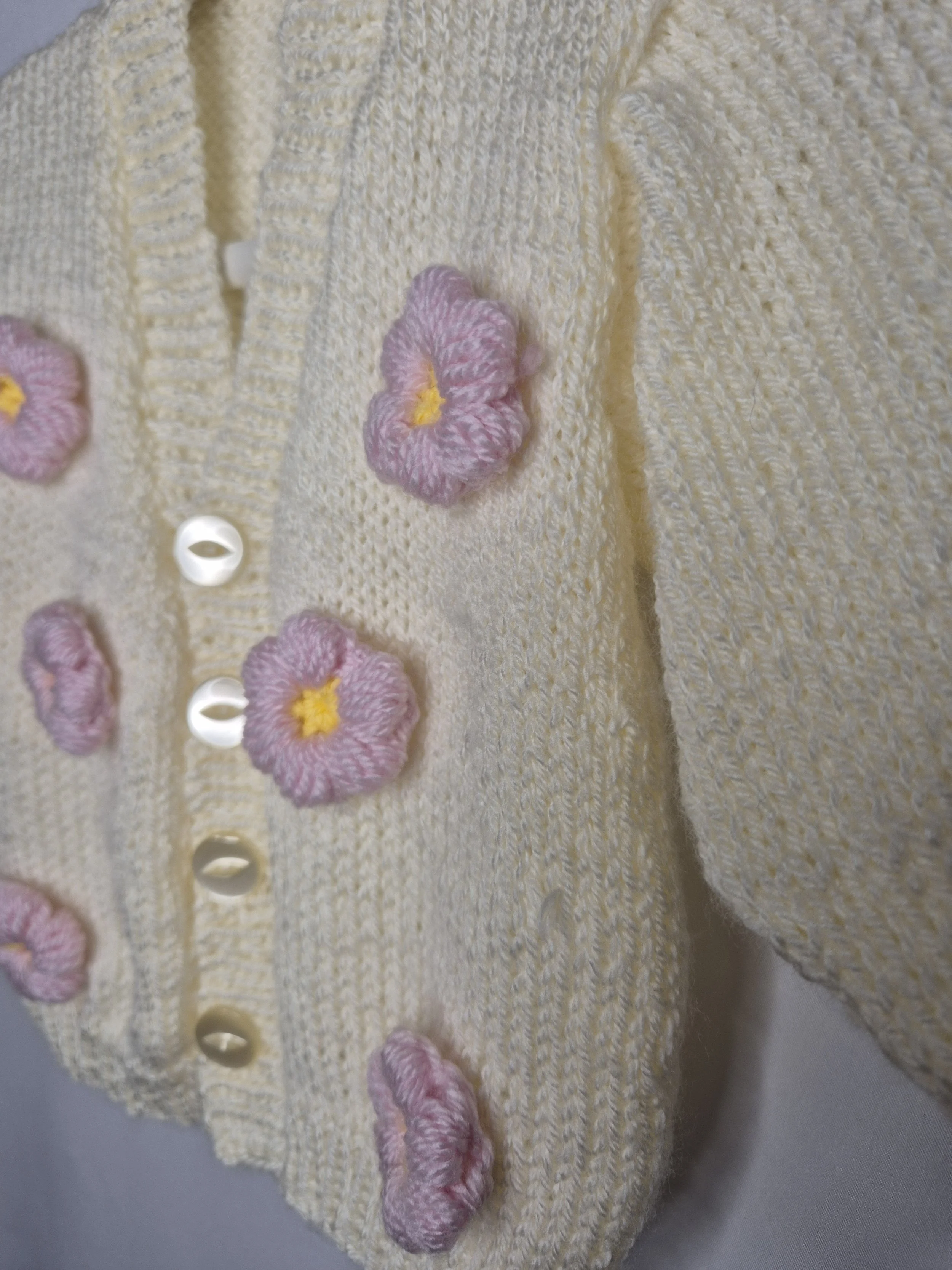 Close-up of a yellow knitted cardigan with pink embroidered flowers and white buttons.