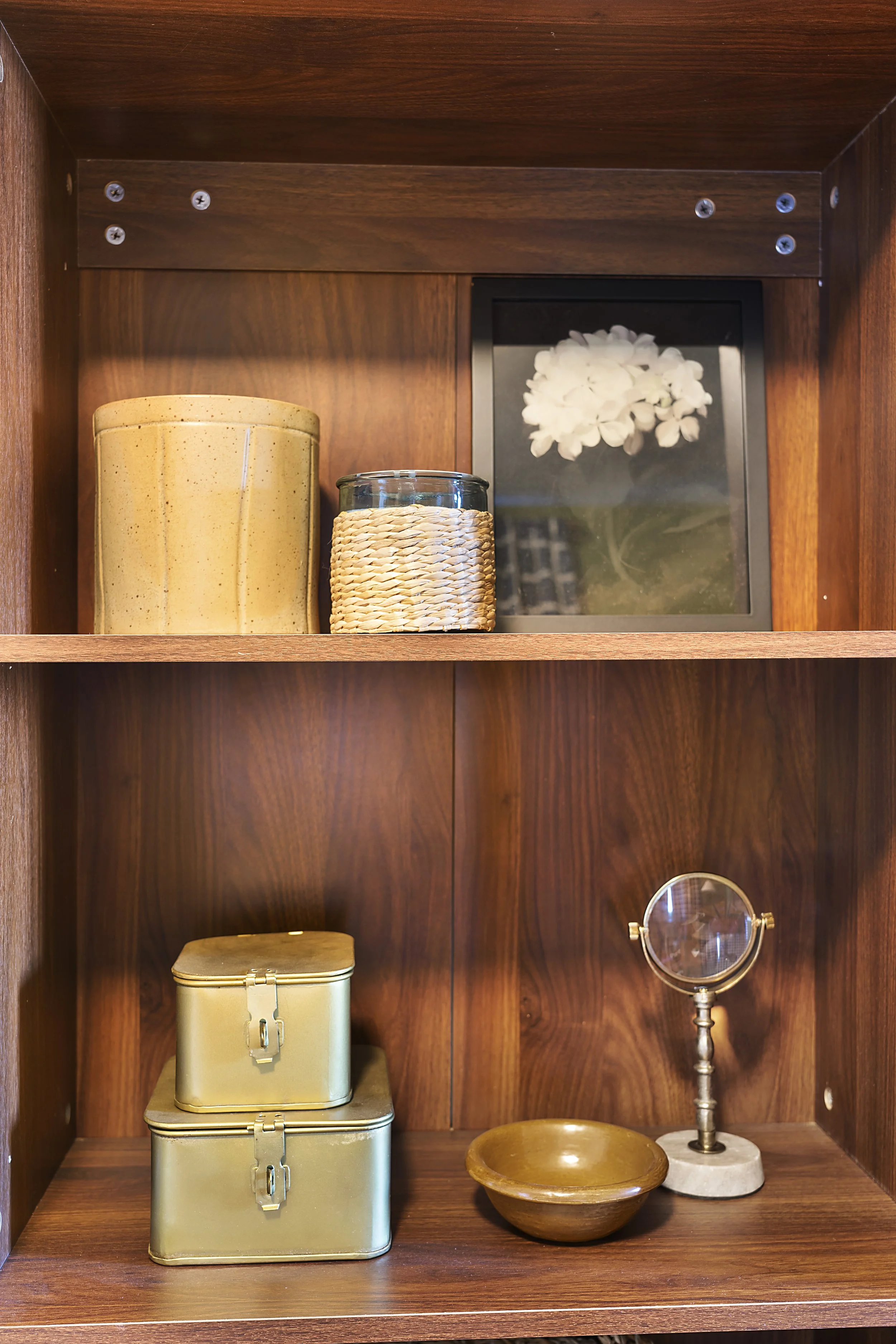 Decorative wooden shelf with containers, a framed flower picture, a bowl, and a magnifying mirror.
