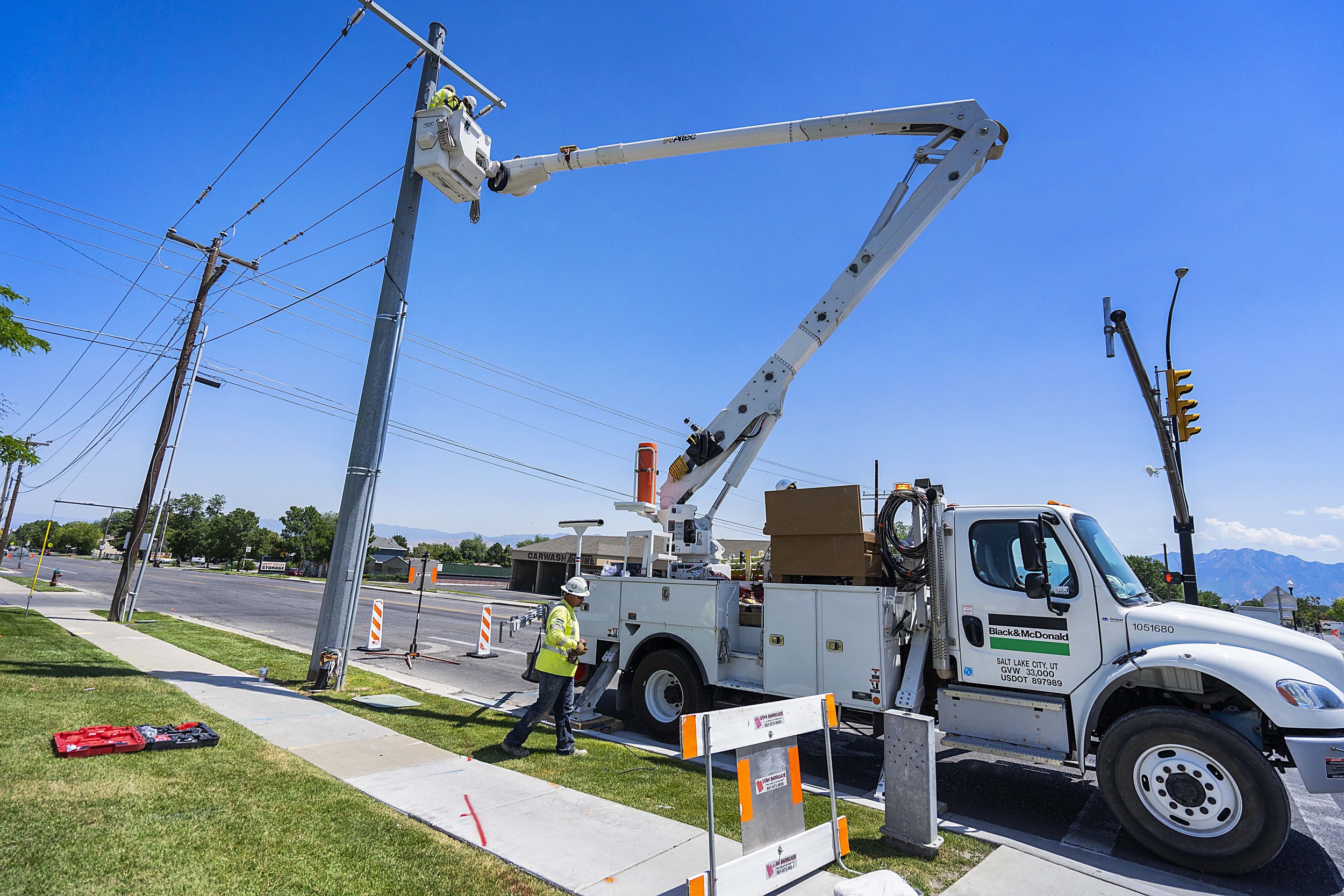 Workers repairing power lines using a bucket truck on a sunny day in a suburban area.