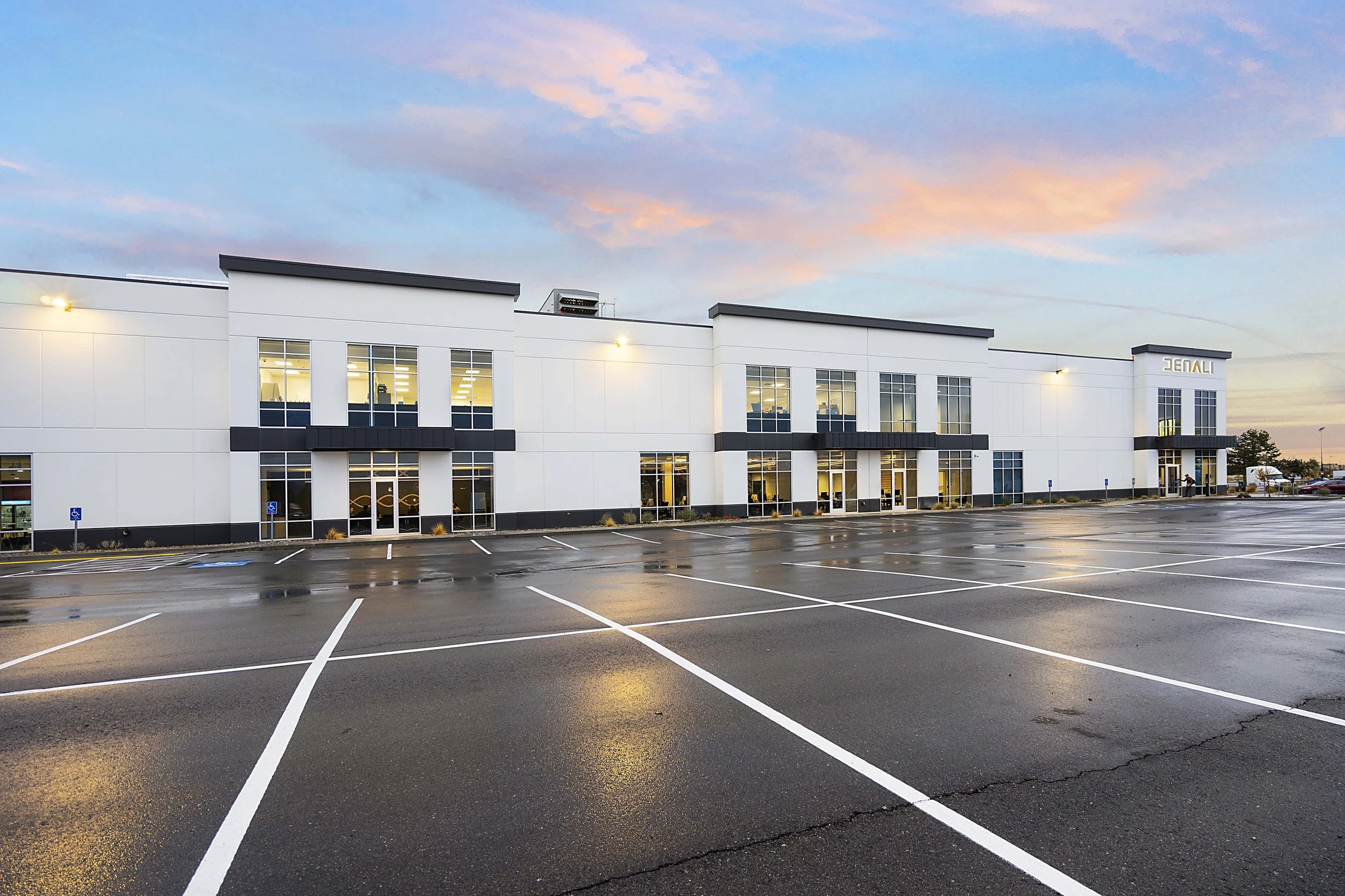 Empty parking lot outside a modern white office building with a sunset sky.