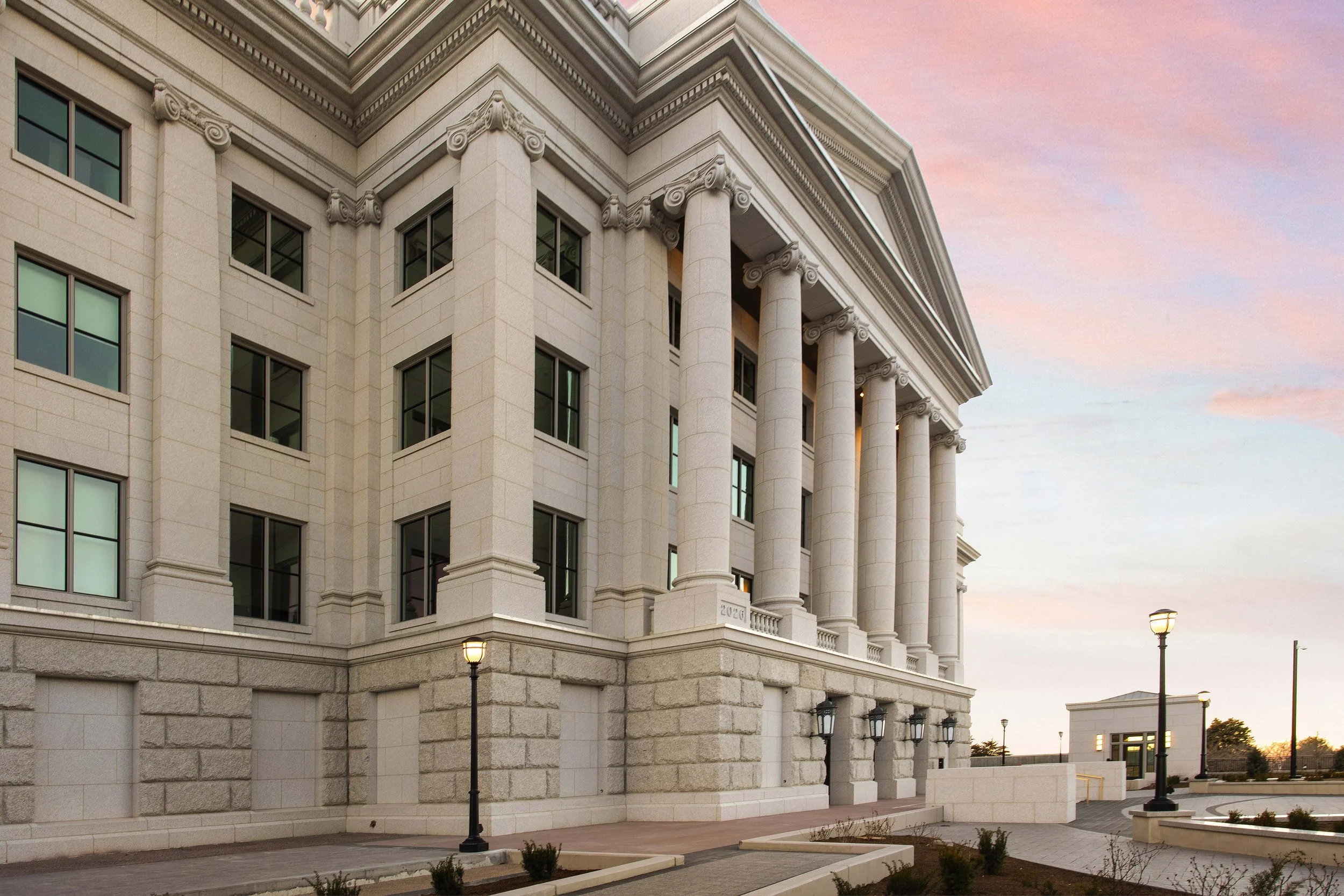 Exterior view of a neoclassical government or institutional building with large columns, stone facade, windows, and street lamps during sunset.