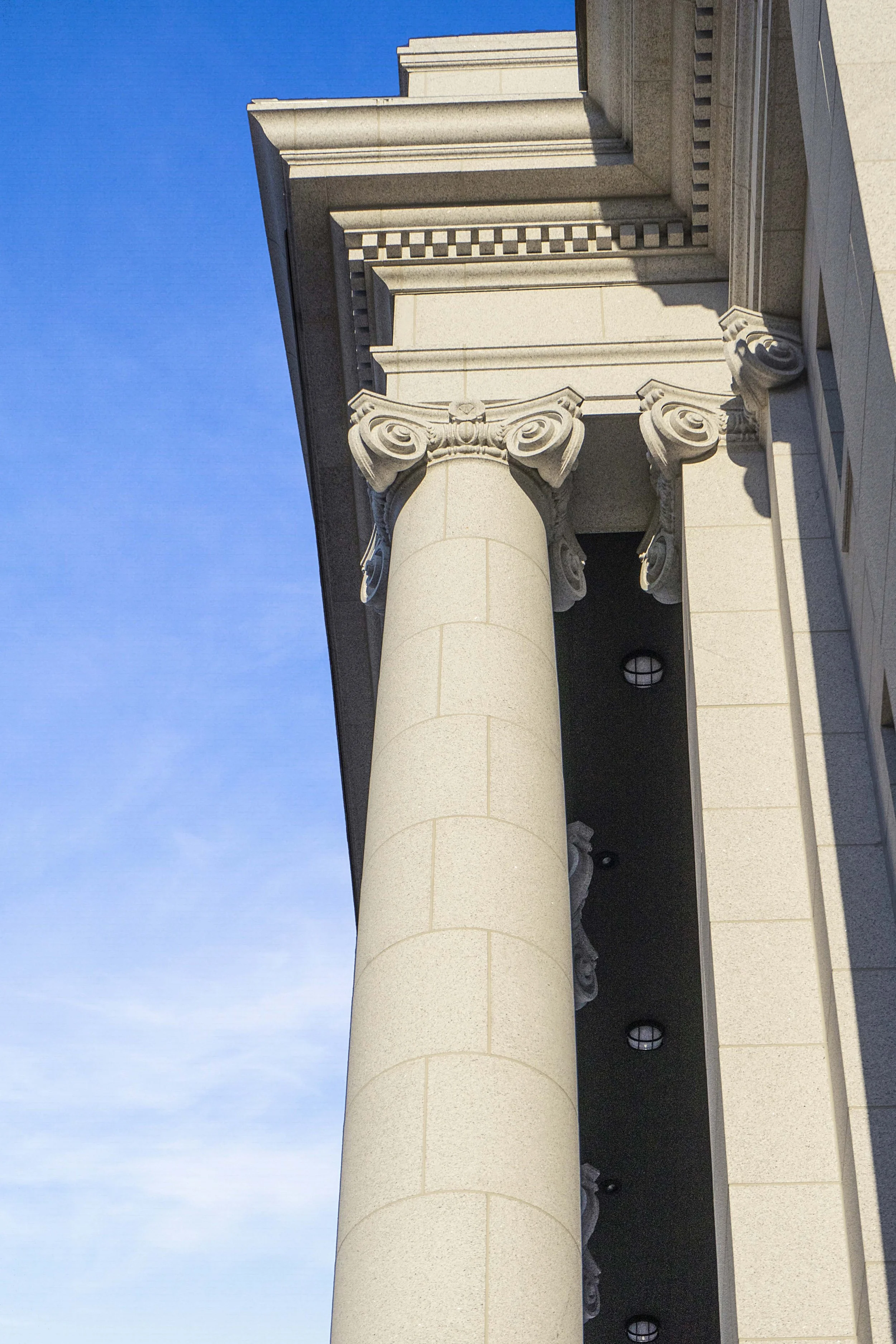 Close-up of a classical architectural column with ornate capital, part of a stately building, against a blue sky.