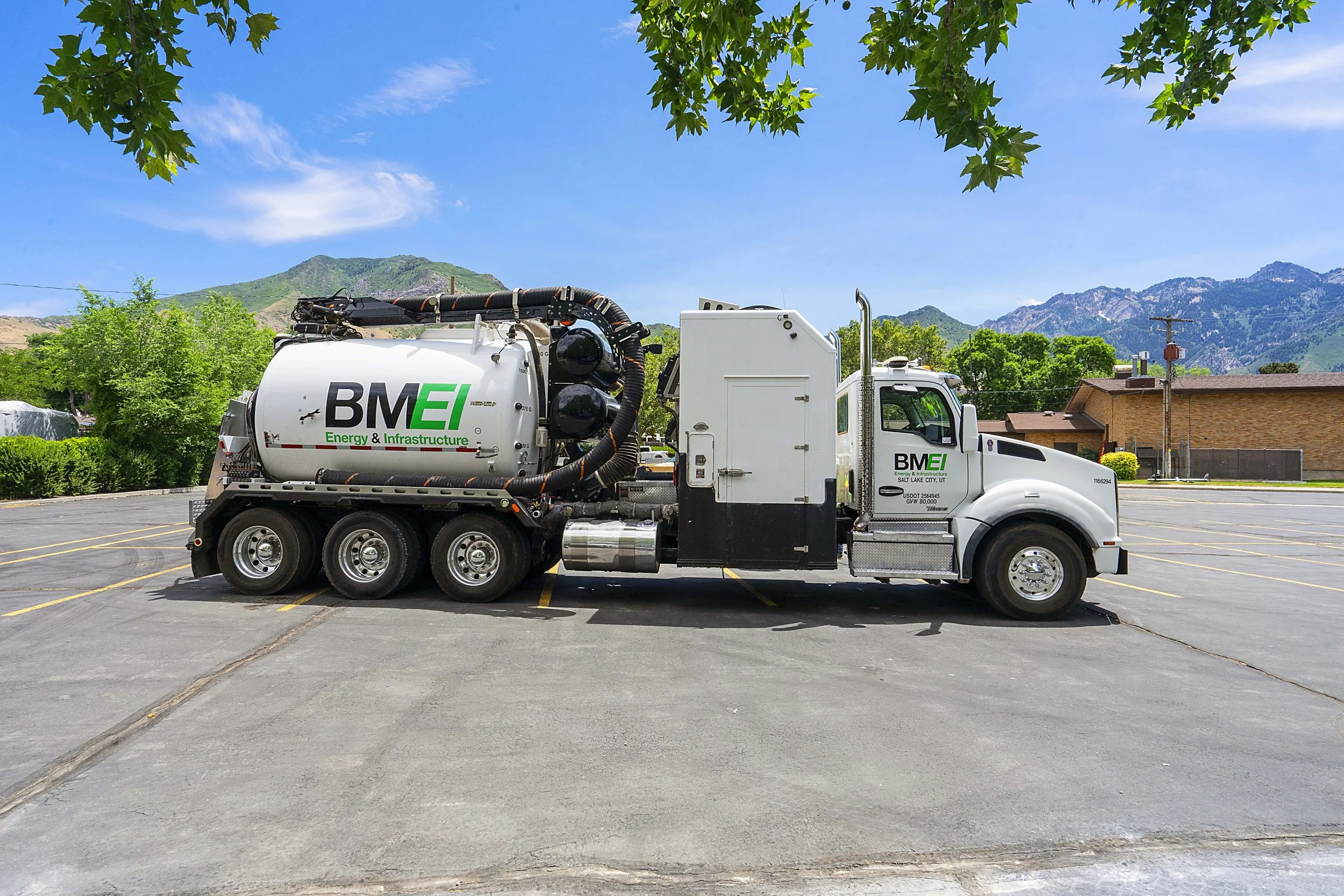 A large white truck labeled 'BMEI Energy & Infrastructure' parked in an empty parking lot with mountains and trees in the background.