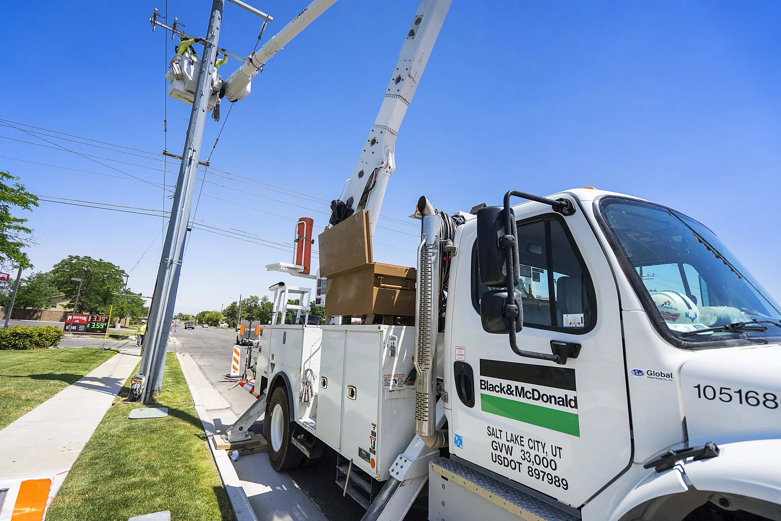 A utility truck with an extension ladder reaching a utility pole on a city street