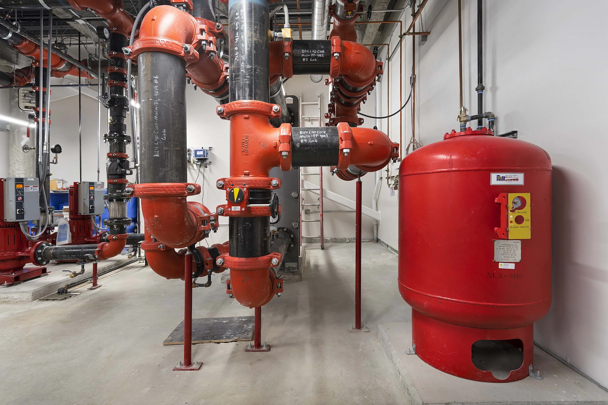 Industrial fire suppression system with large red tanks and network of red and black pipes.