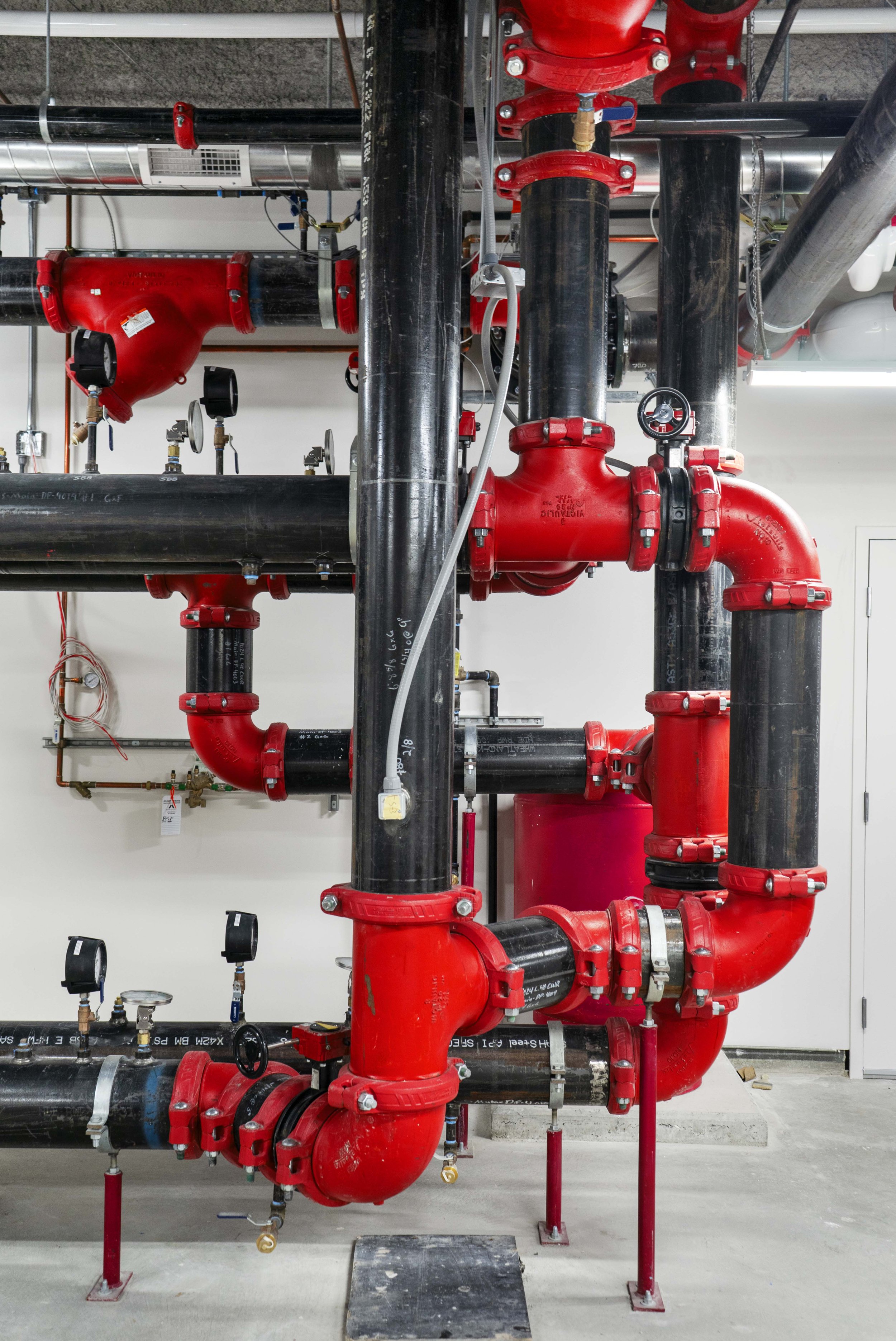 Industrial piping system with black pipes and red fittings, including valves and gauges, installed indoors.
