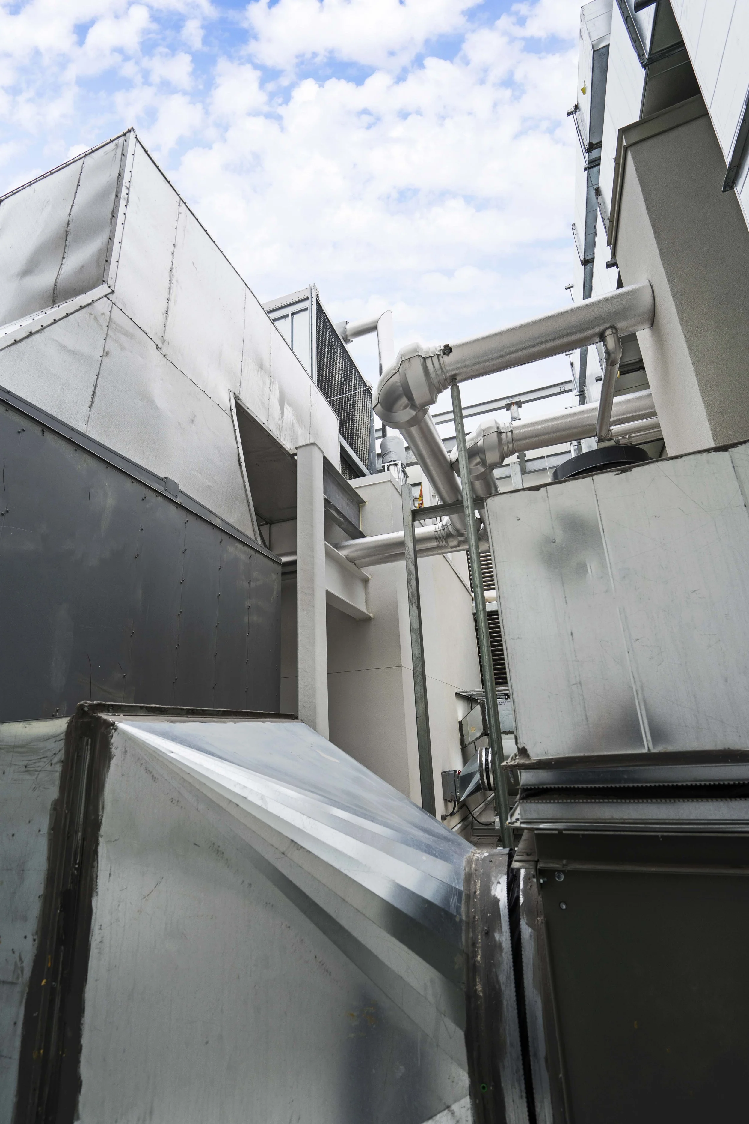 View of industrial rooftop with metallic HVAC units, pipes, and ducts against a blue sky with clouds.
