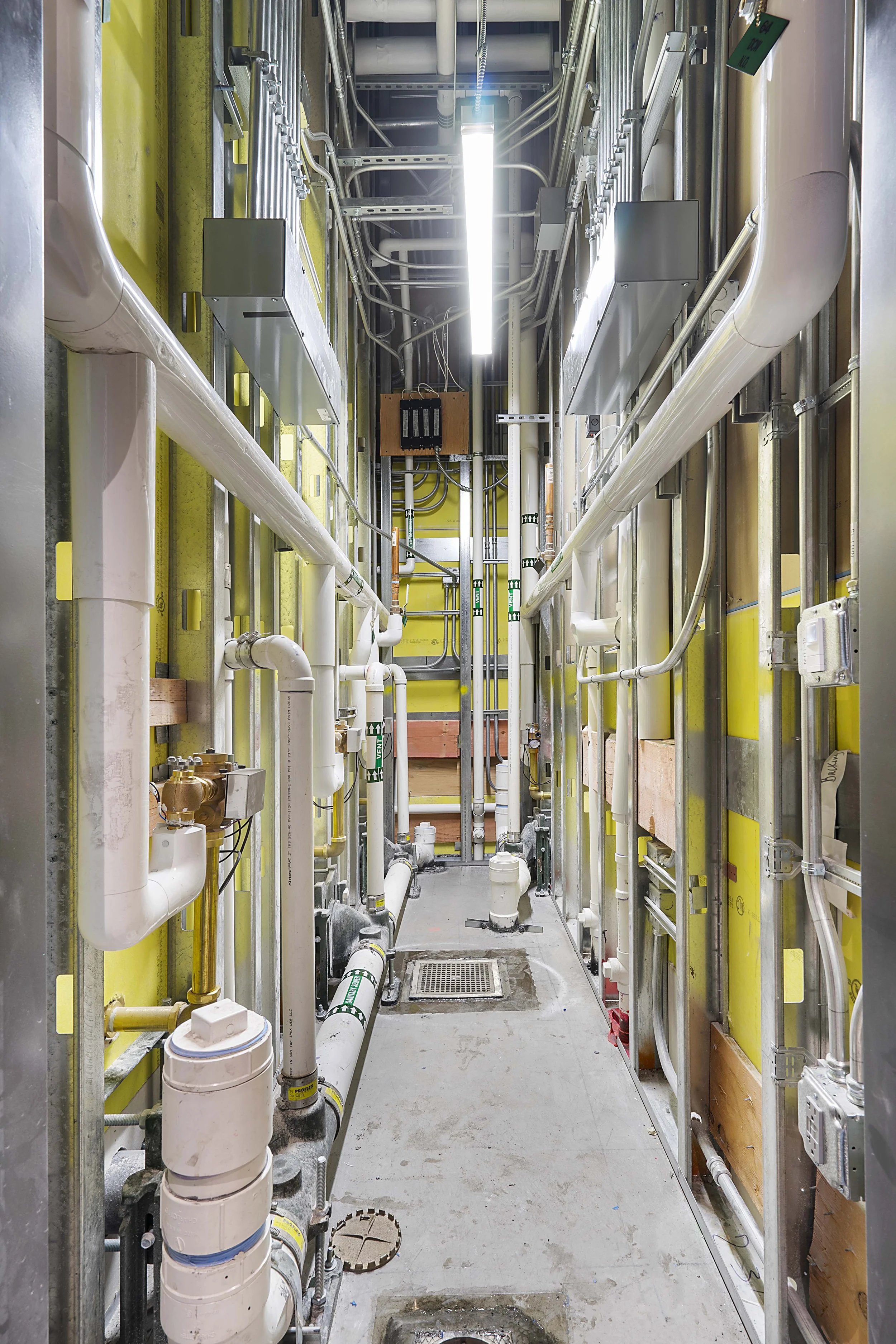 An industrial utility room with various pipes, conduit, and electrical panels.