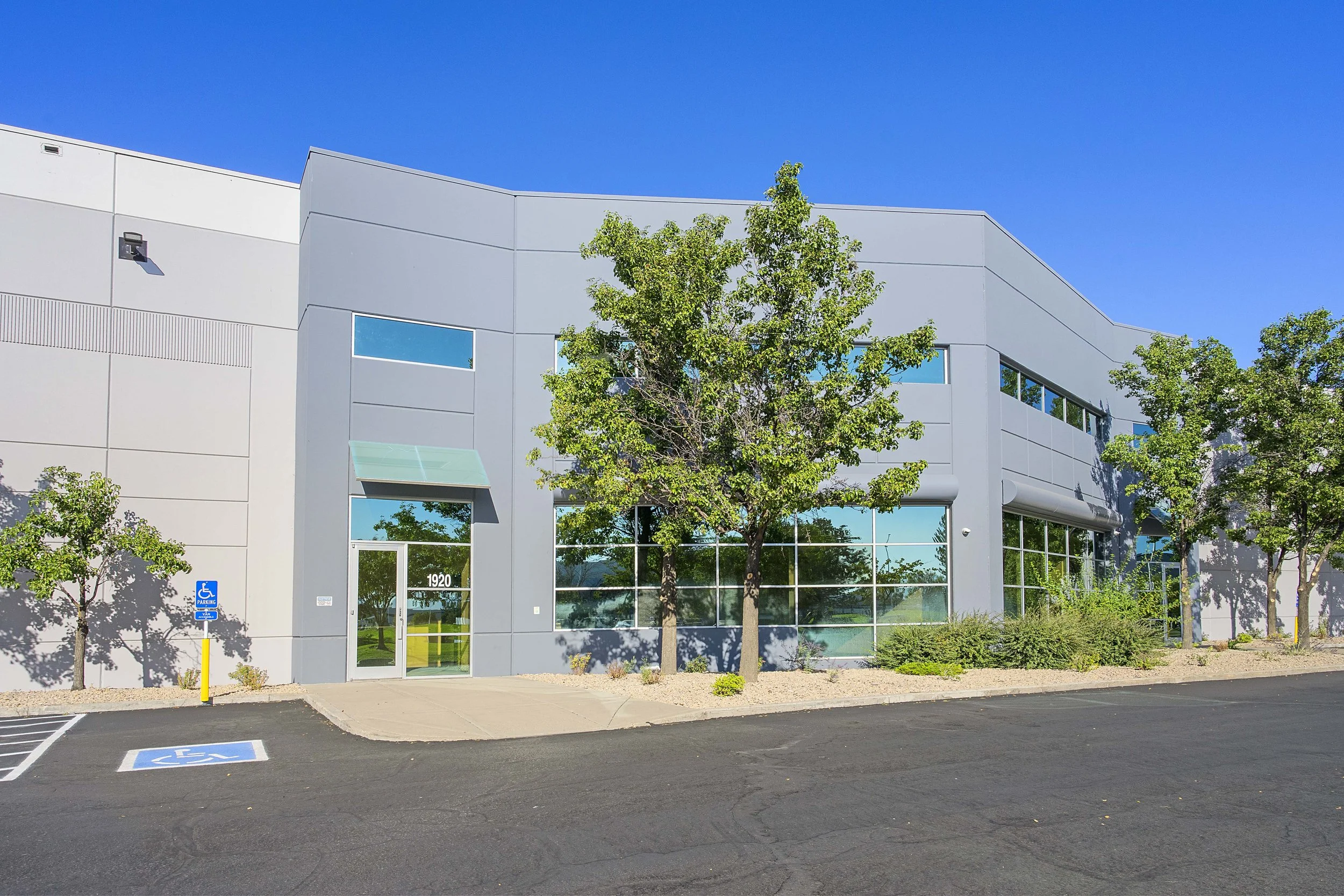 Modern commercial building with large glass windows, trees, parking lot, and a handicapped parking space in front