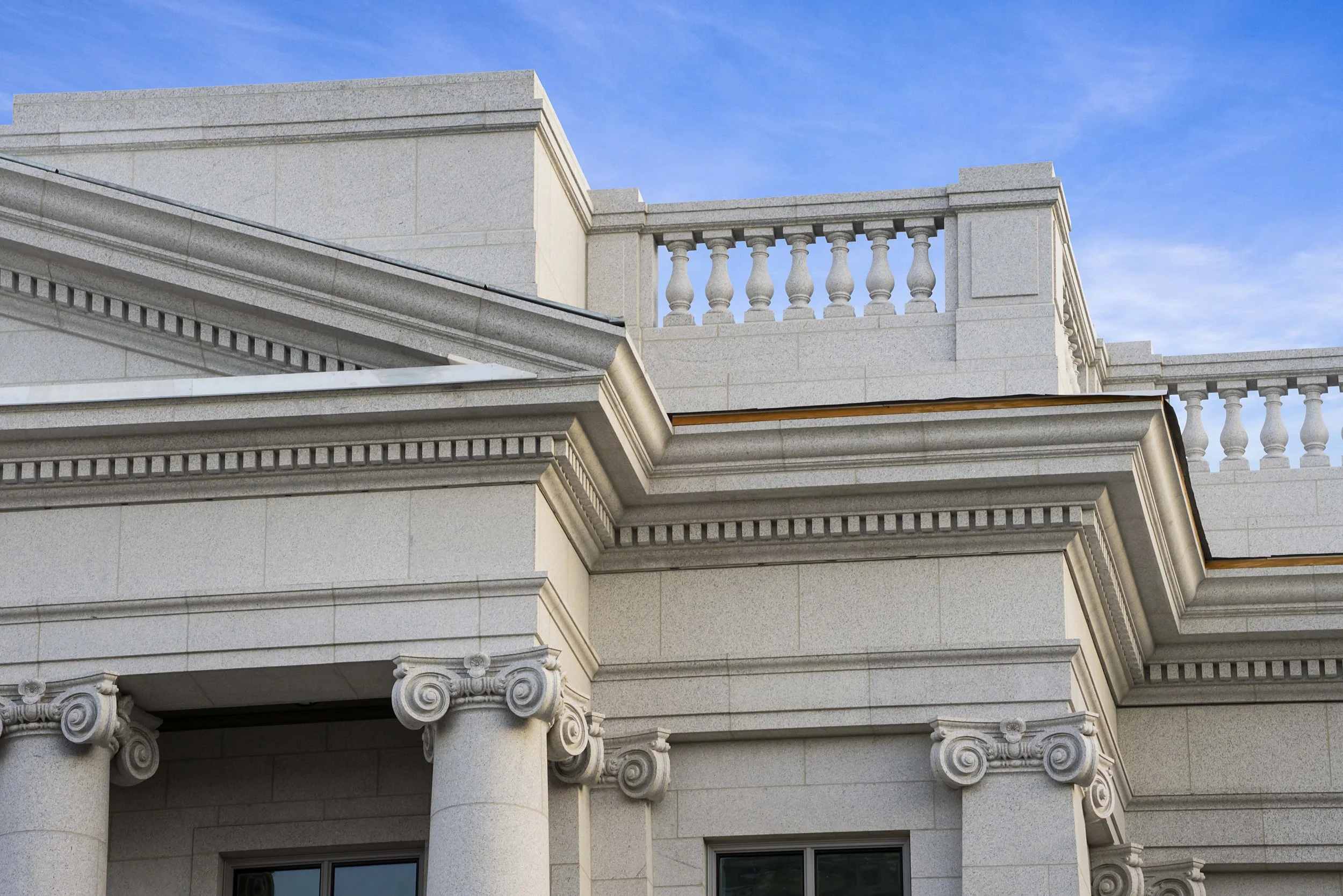 Close-up of a classical building facade with ornate columns, decorative molding, and stone balcony railings against a blue sky.