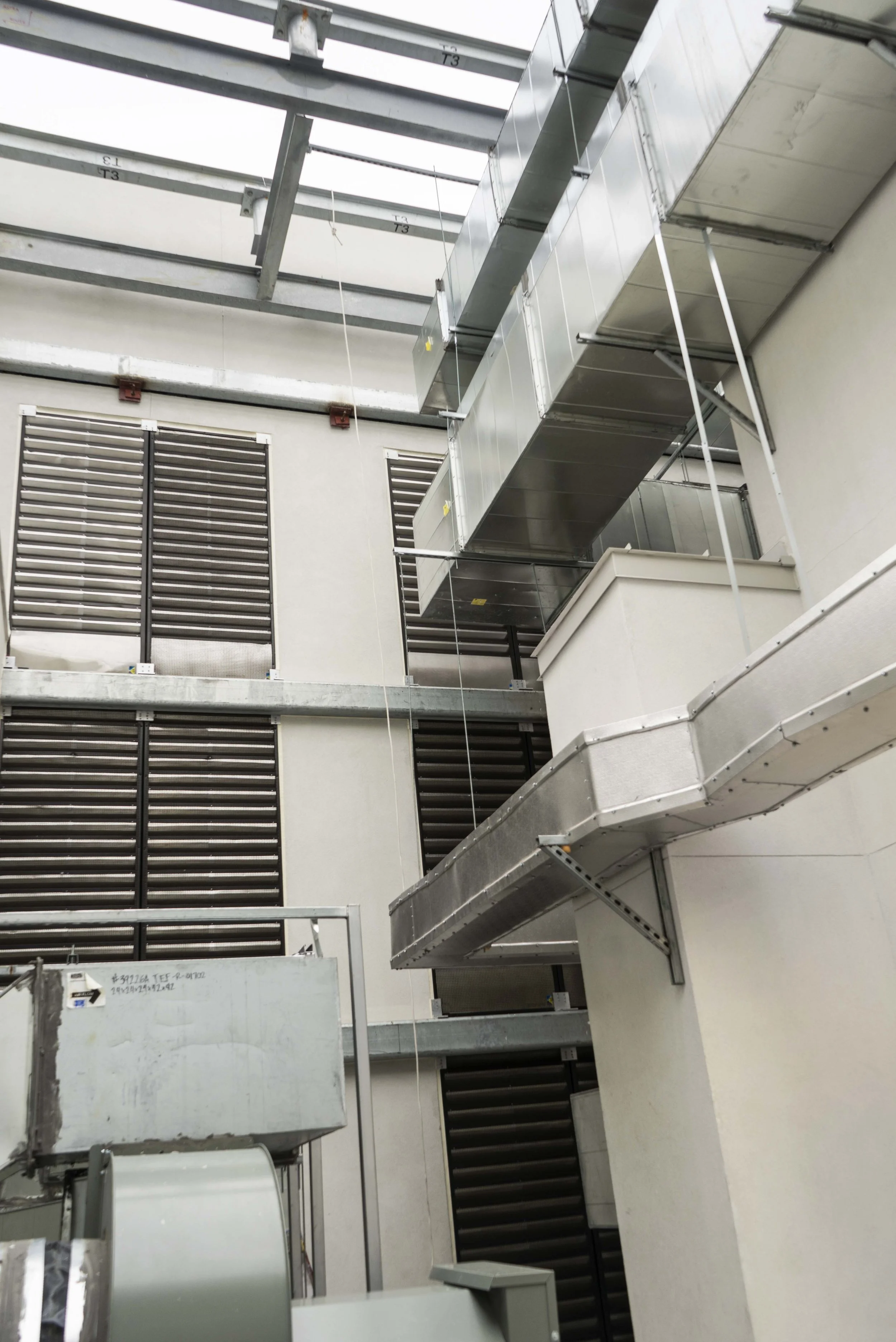 Interior view of a building under construction with exposed HVAC ductwork, metal framework, and vents on the walls and ceiling.