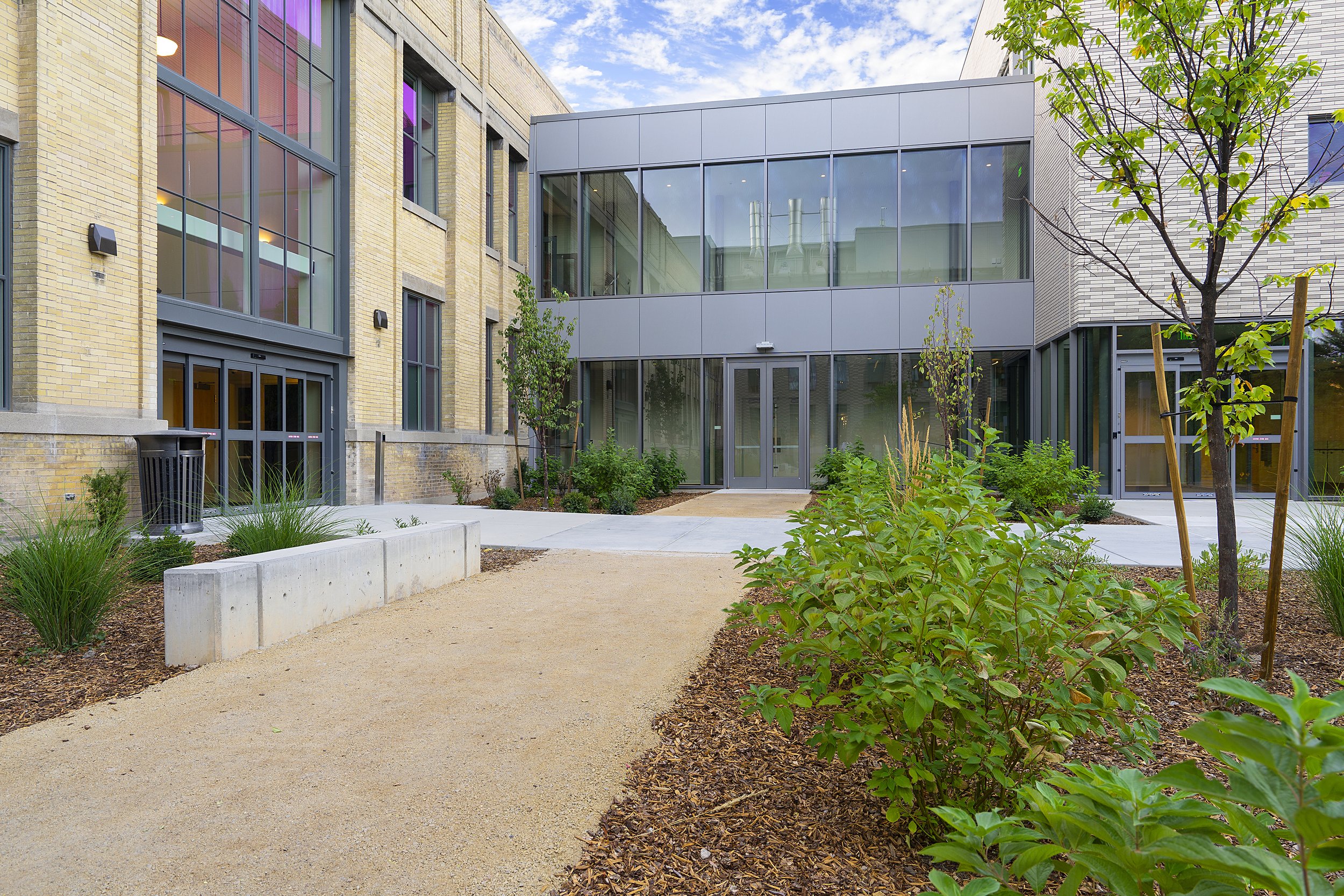 Modern building with glass windows and a landscaped courtyard with trees and shrubs.