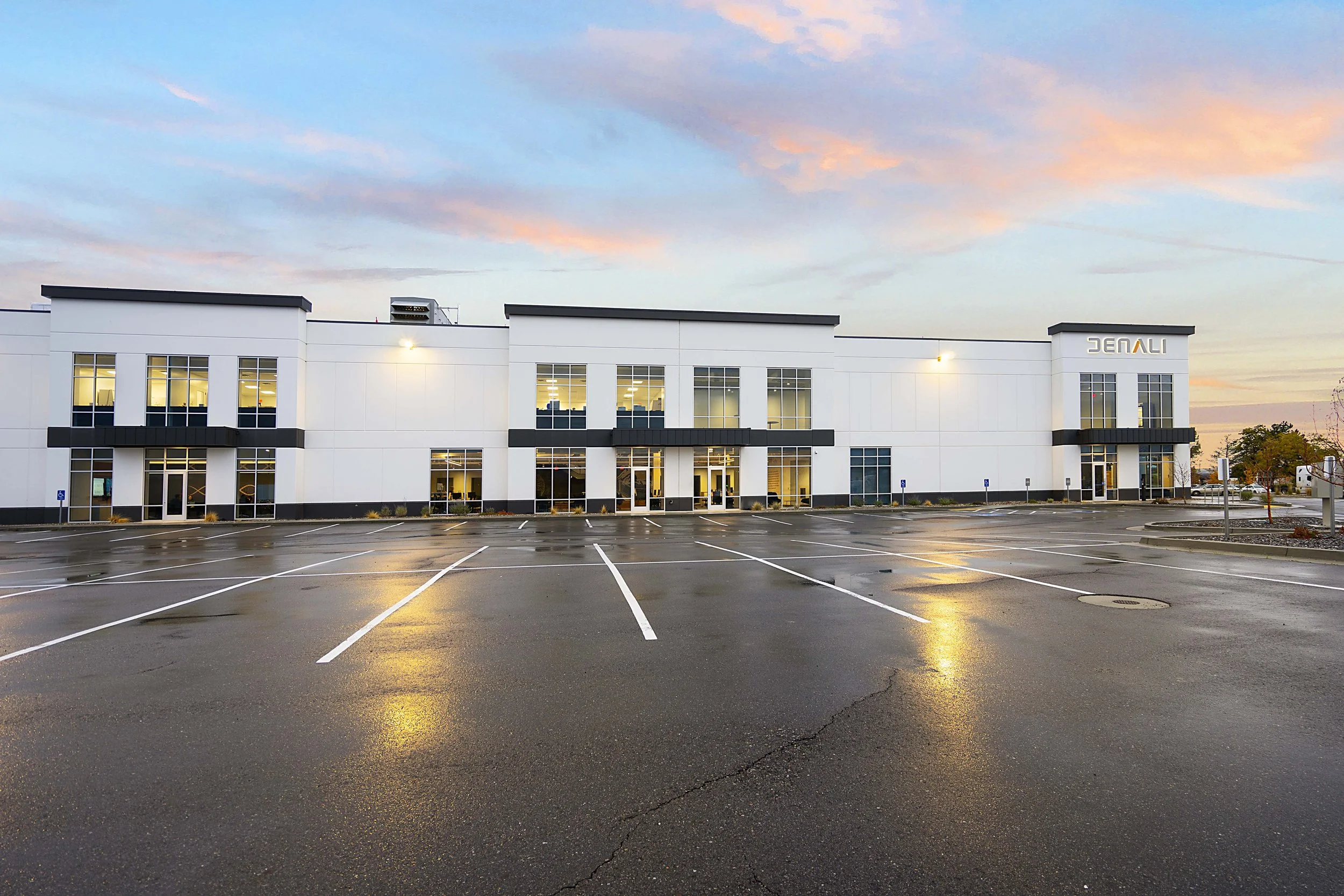 Empty parking lot in front of a modern white office building with large windows at sunset.