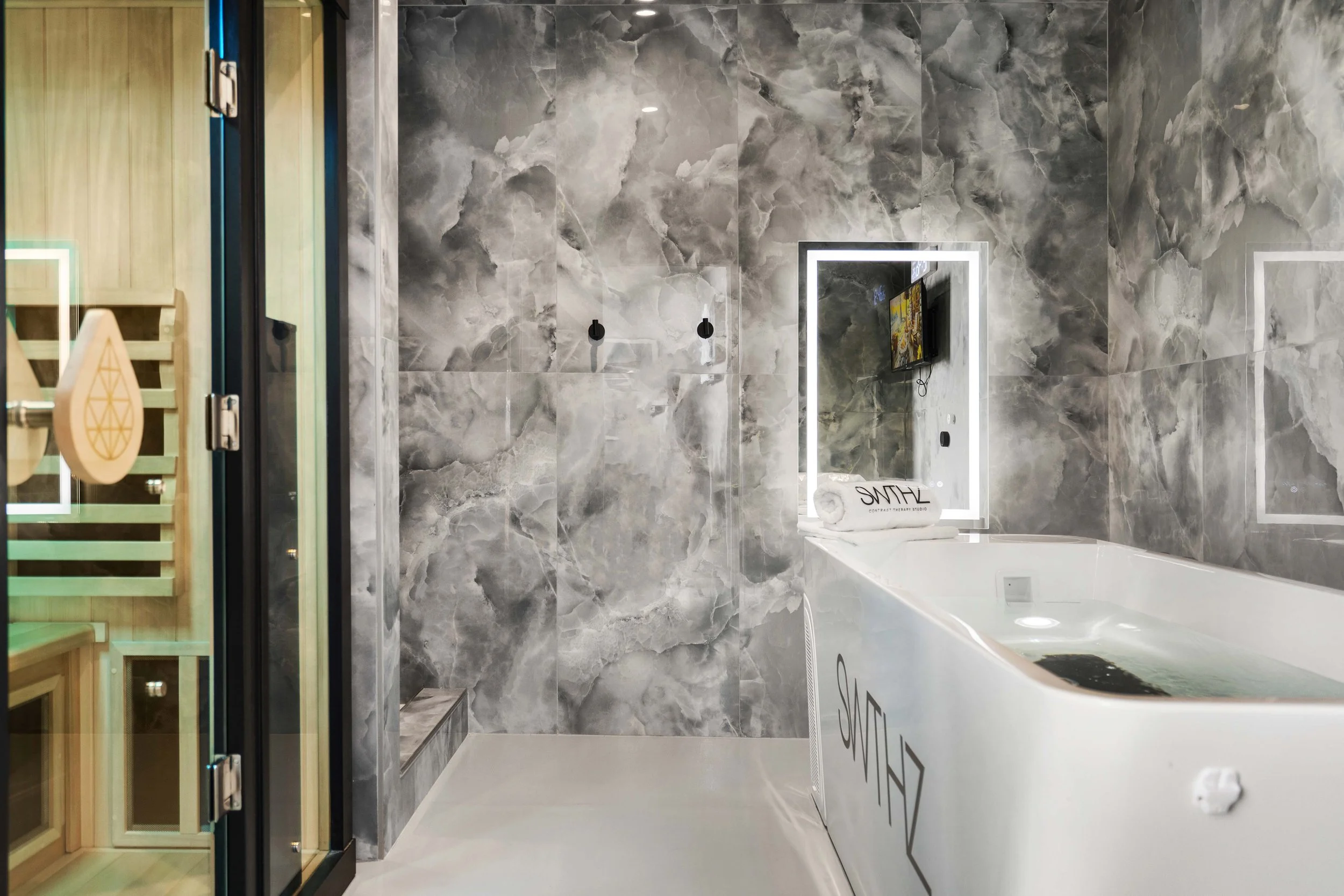 Modern bathroom with gray marble walls, a white bathtub, and a mirror with LED lighting.