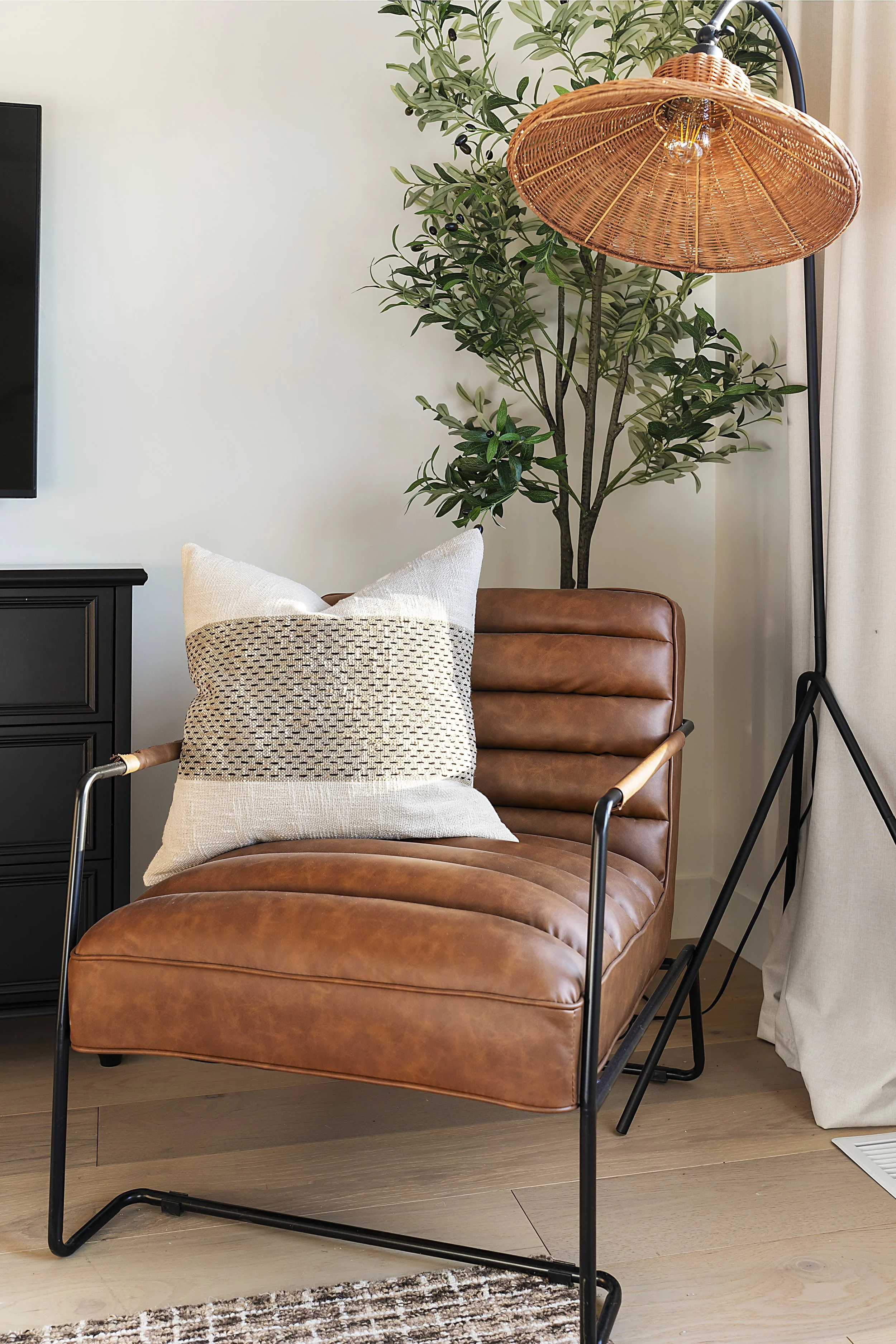 Living room scene with a leather lounge chair, decorative pillow, potted plant, and a floor lamp with a woven shade.