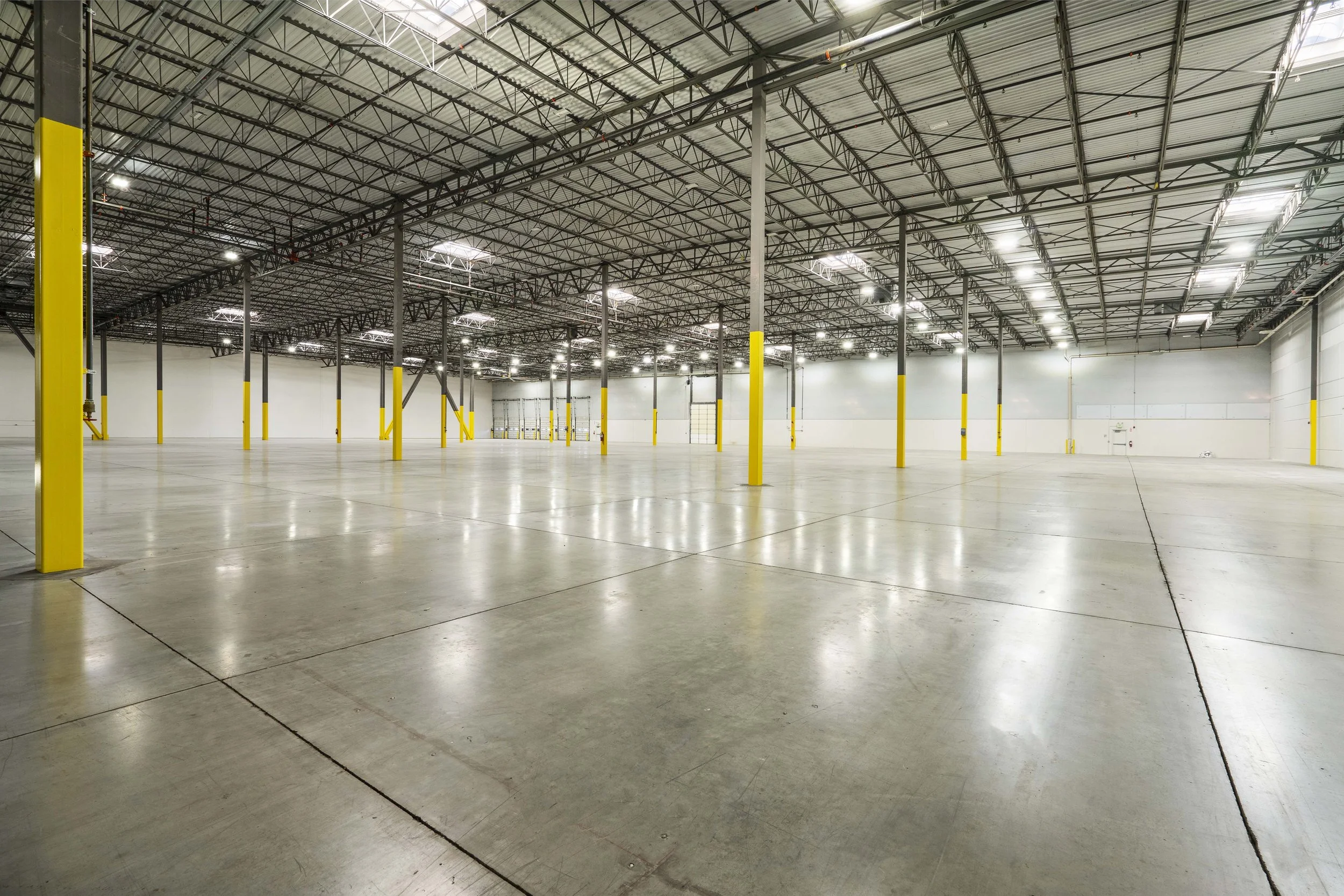 Empty warehouse with yellow safety posts, metal ceiling, and bright overhead lighting.