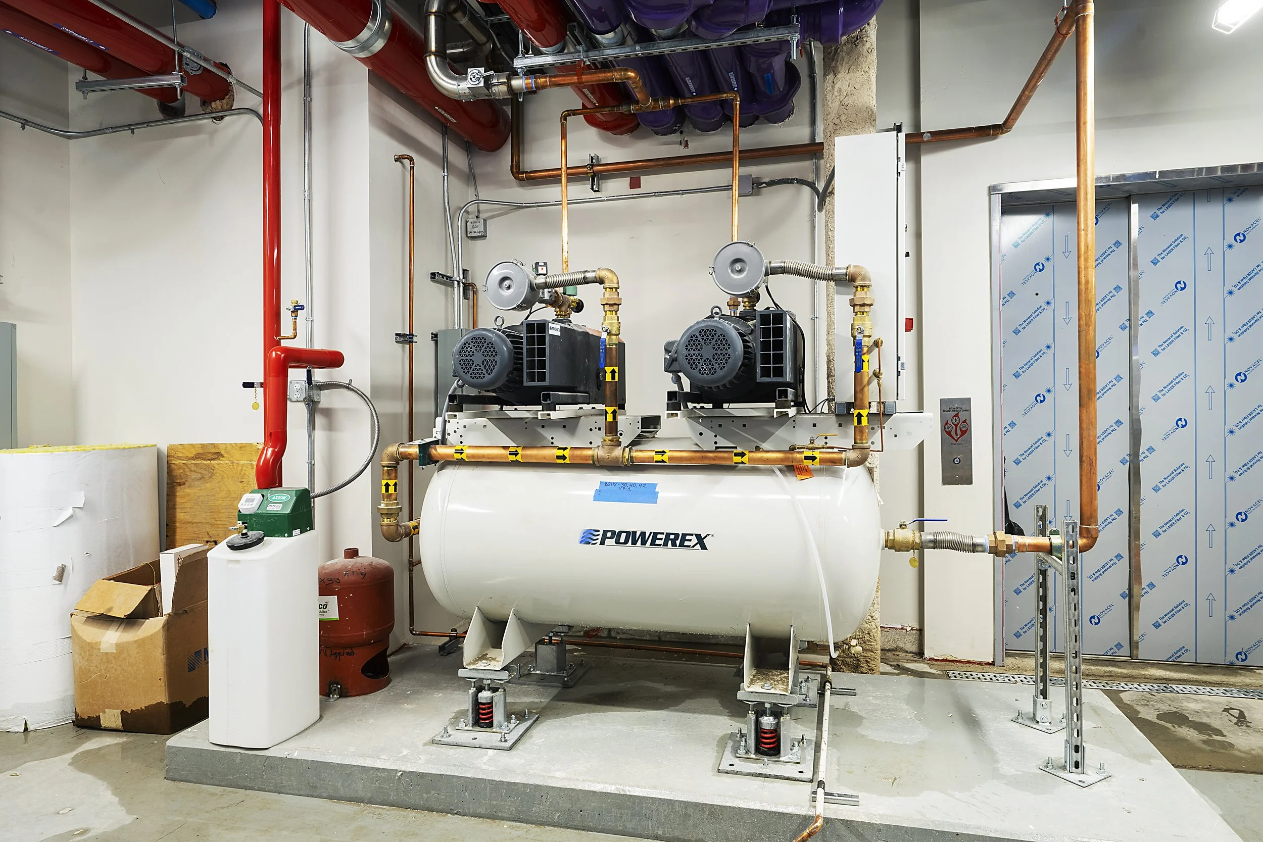 Industrial air compressor with copper pipes and electrical components in a mechanical room.