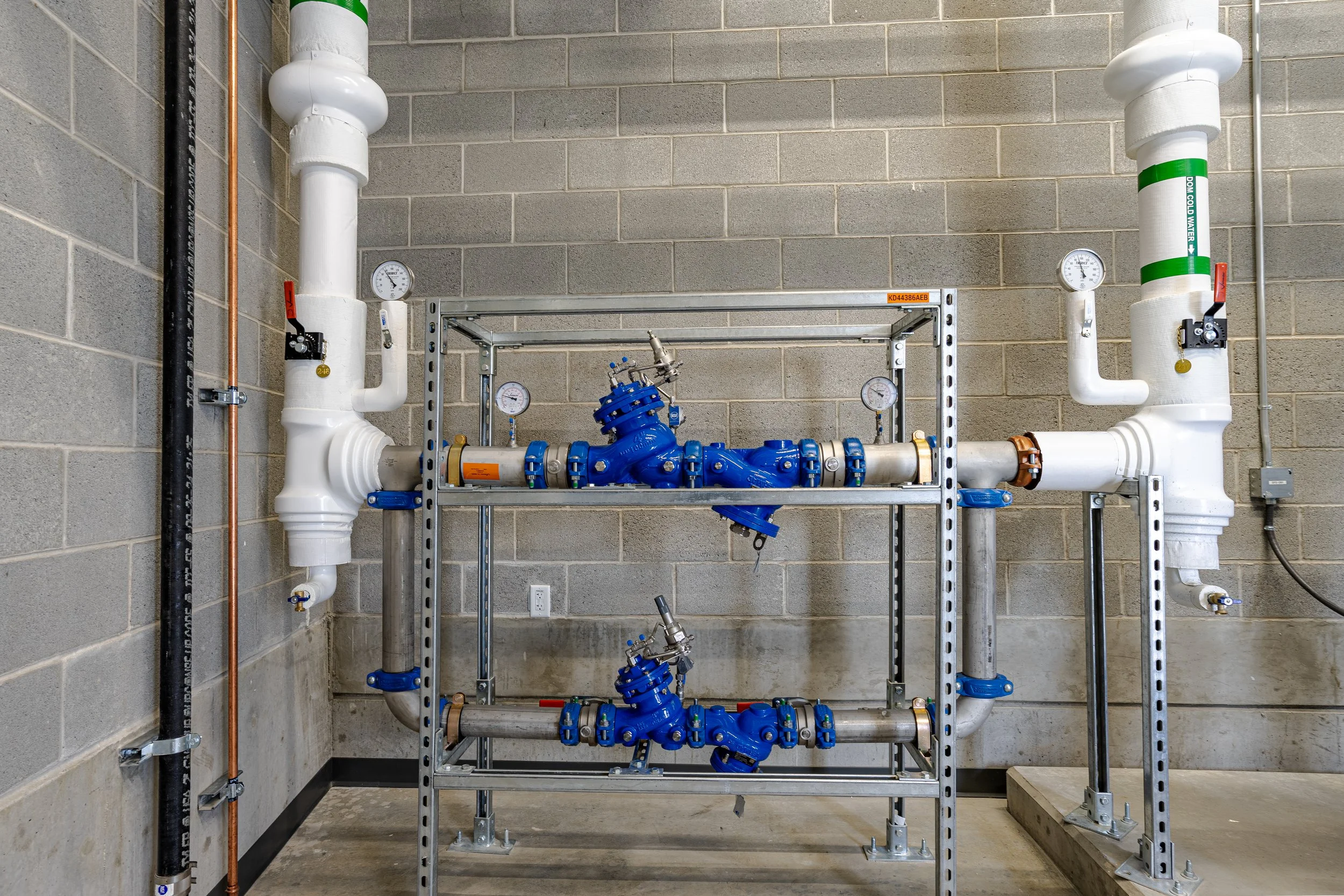 Industrial piping system with valves, gauges, and a blue pump mounted on a metal framework in a warehouse