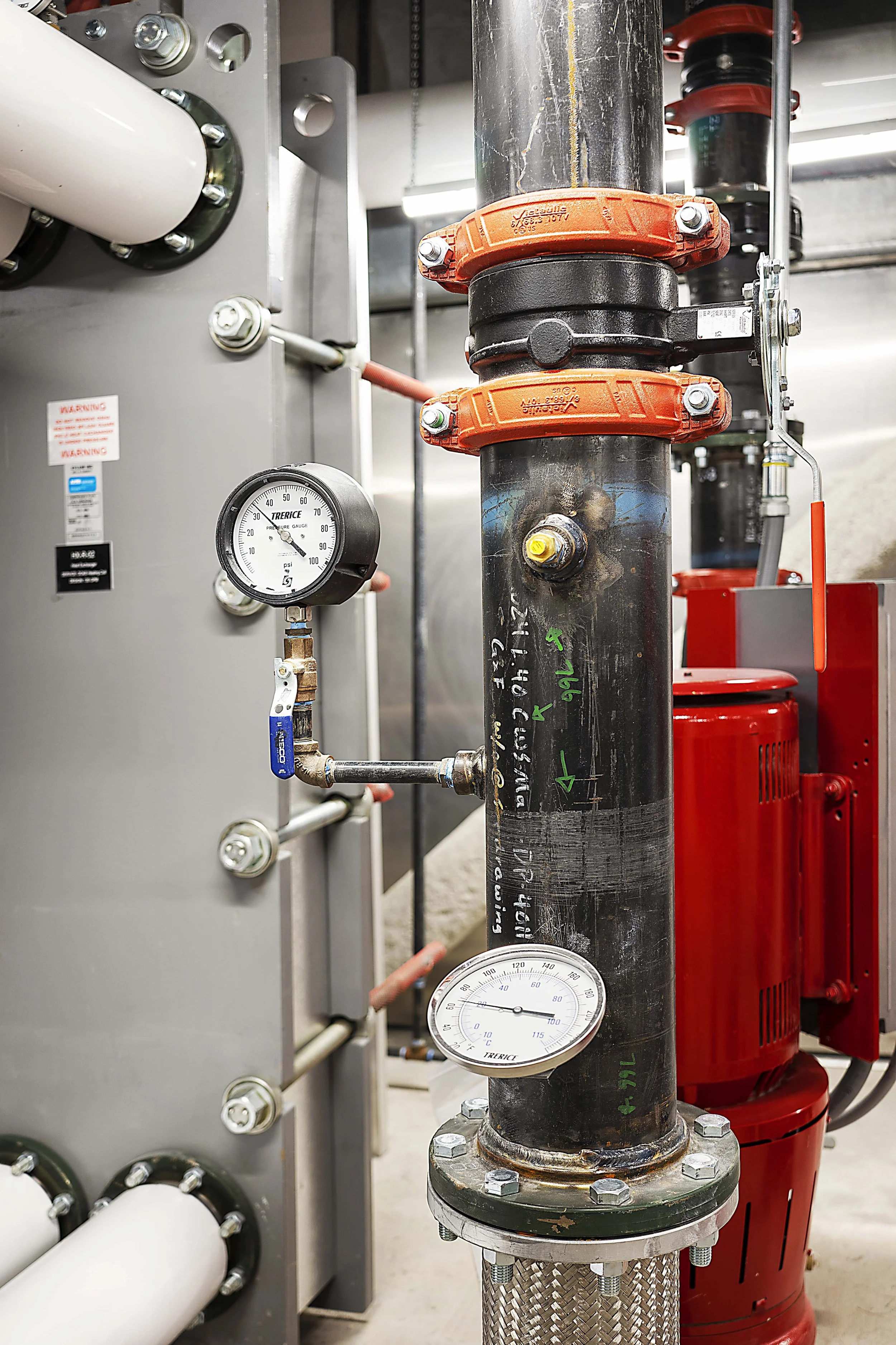 Industrial plumbing system with gauges, pipes, and valves in a mechanical room.