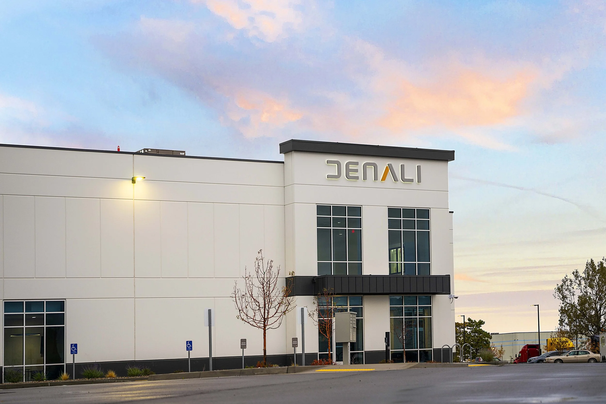 An exterior view of a modern building with a sign that reads 'JENALI' against a pastel sky at sunset.
