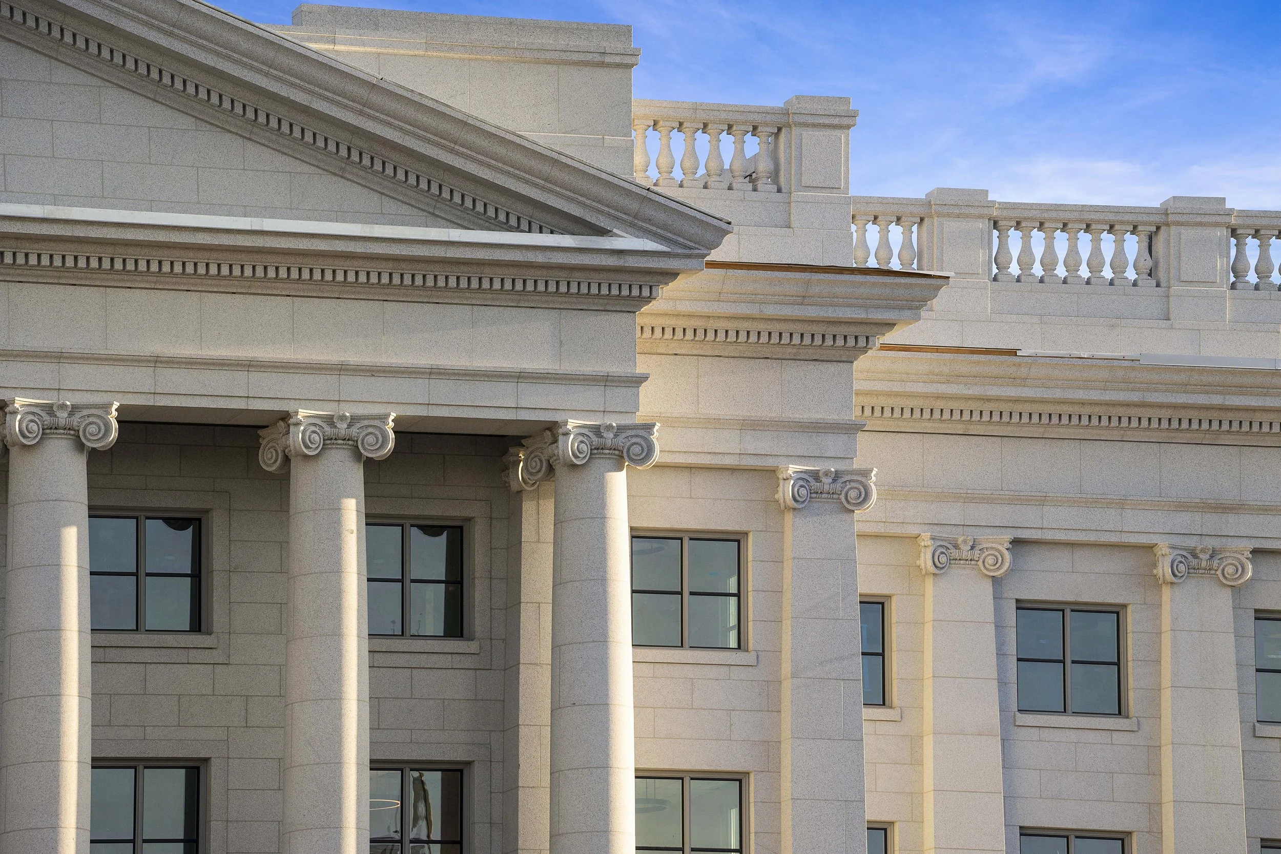 Close-up of classical-style building with columns, decorative capitals, and balustrade against blue sky.