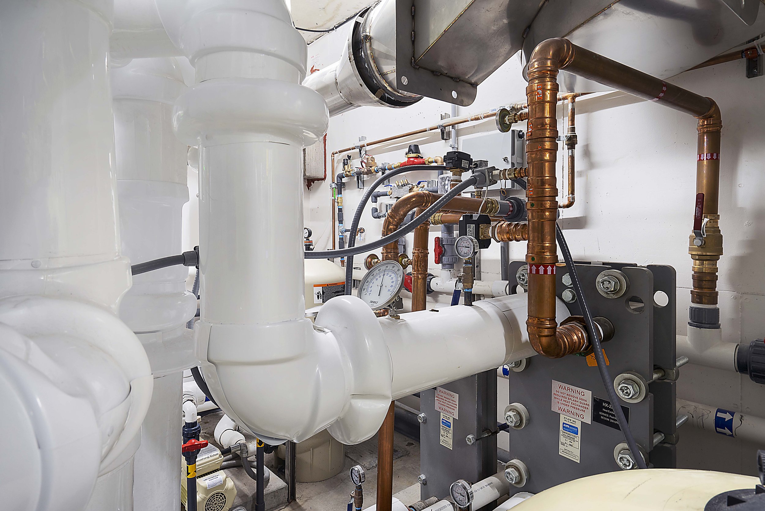 A mechanical room with a complex system of white pipes, copper pipes, gauges, and valves.