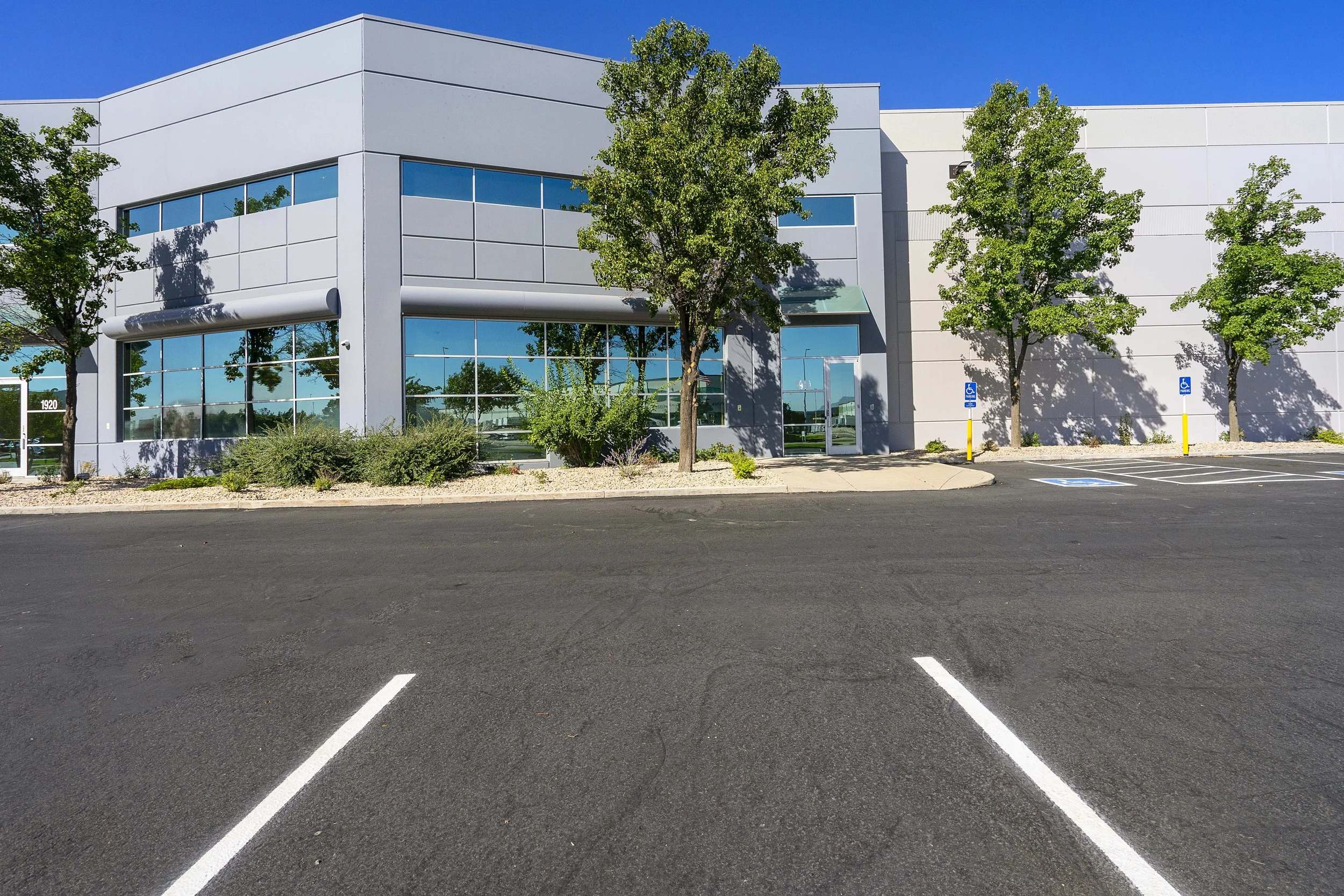 Empty parking lot in front of a modern office building with trees and clear blue sky.