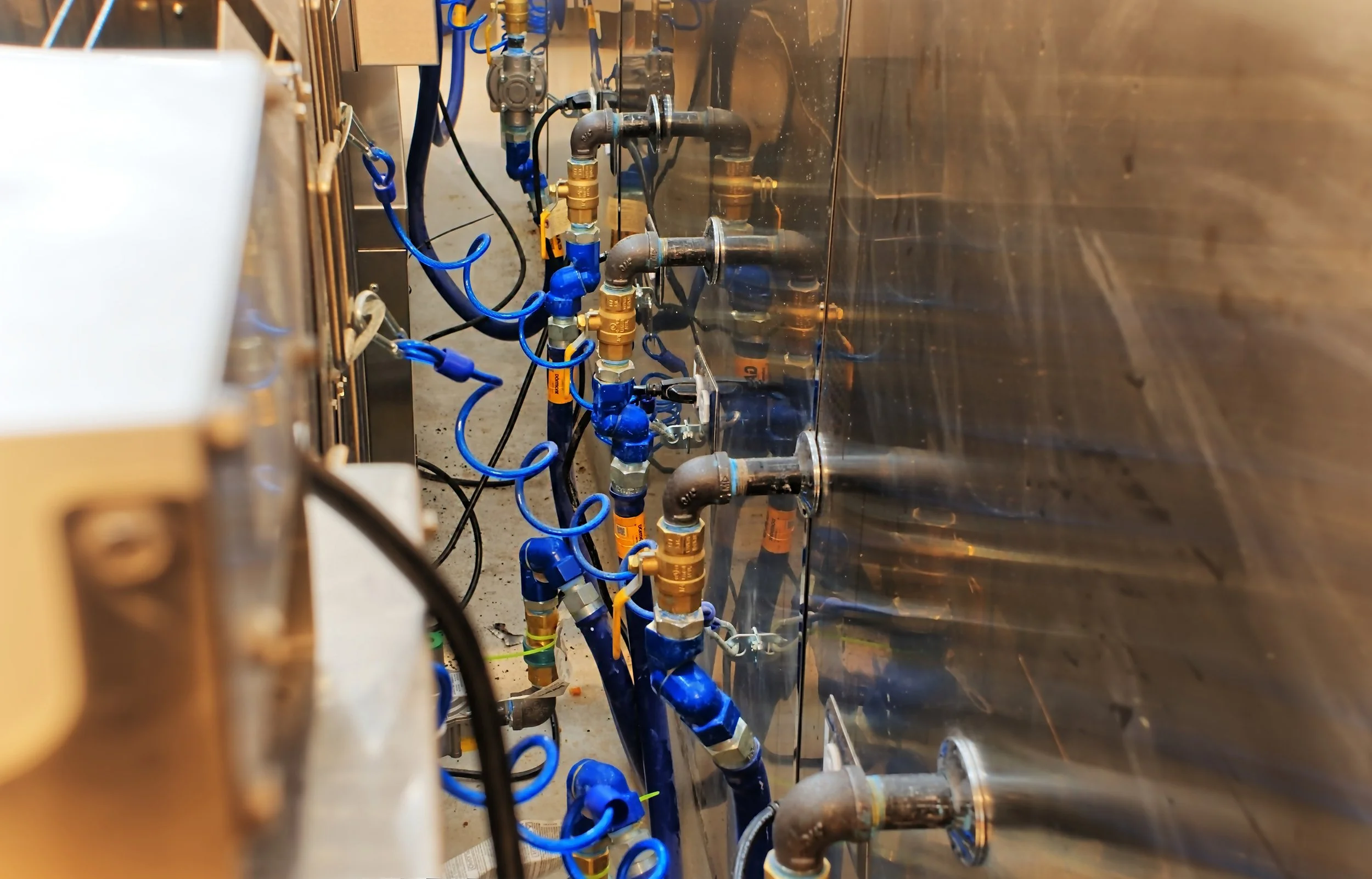 Pipes and valves connected to a stainless steel tank, with blue and black hoses and brass fittings.