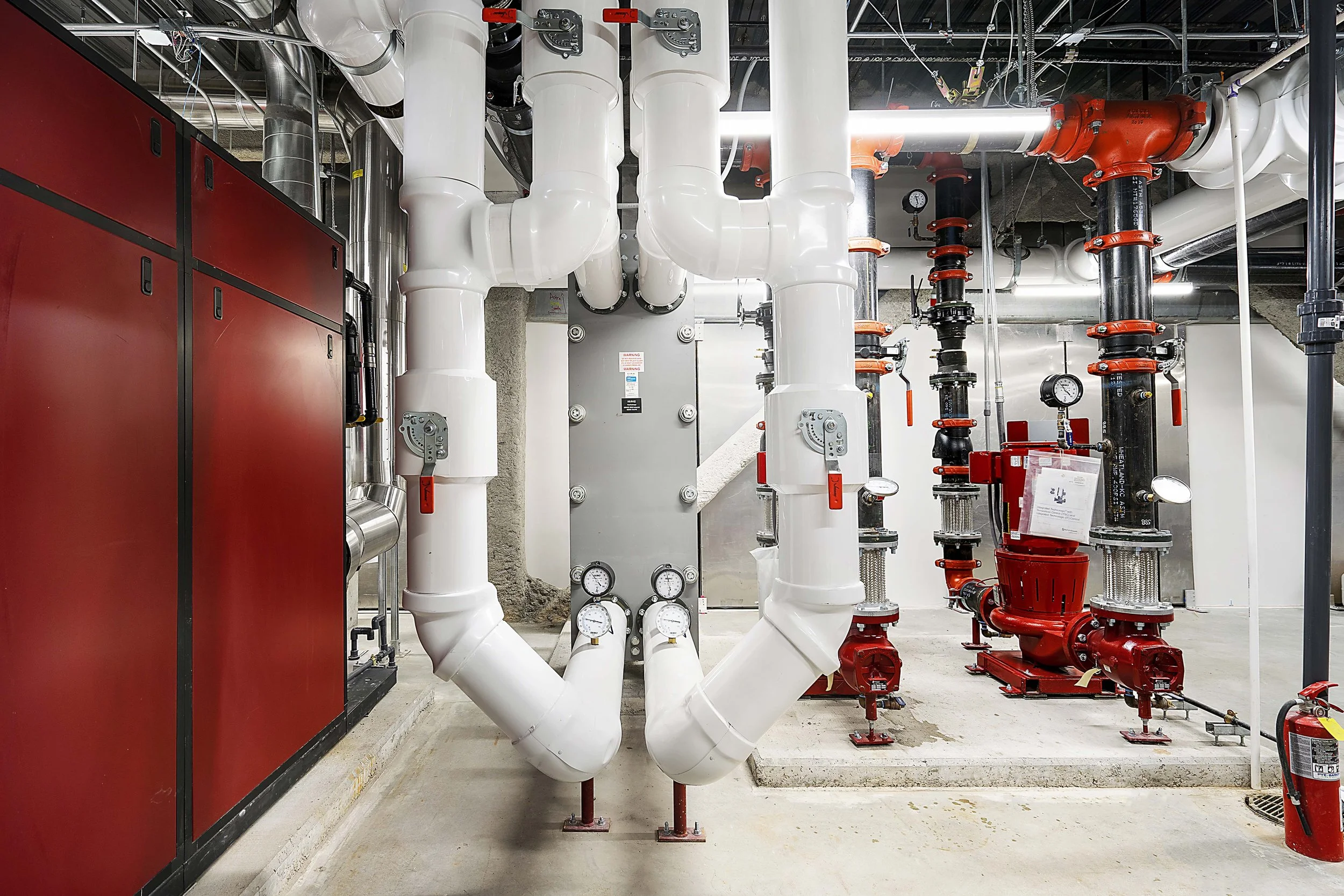 Industrial mechanical room with white and red pipes, gauges, and large equipment.