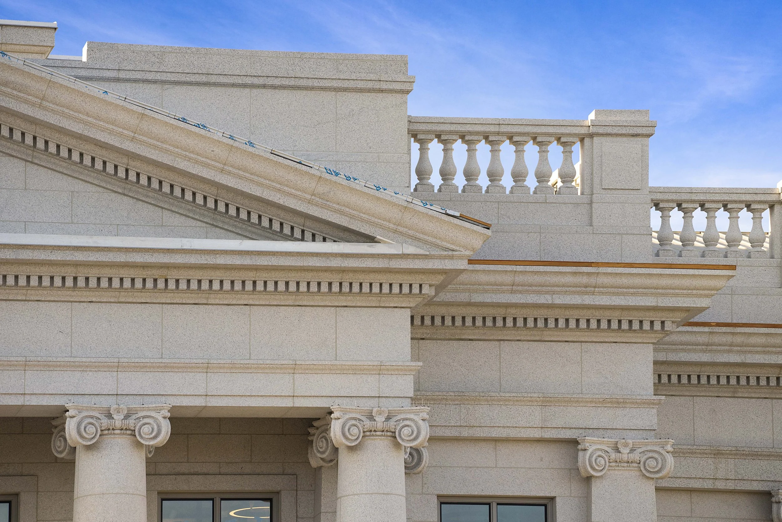 Close-up of classical architectural features on a building, including columns, decorative molding, and balustrades against a blue sky.