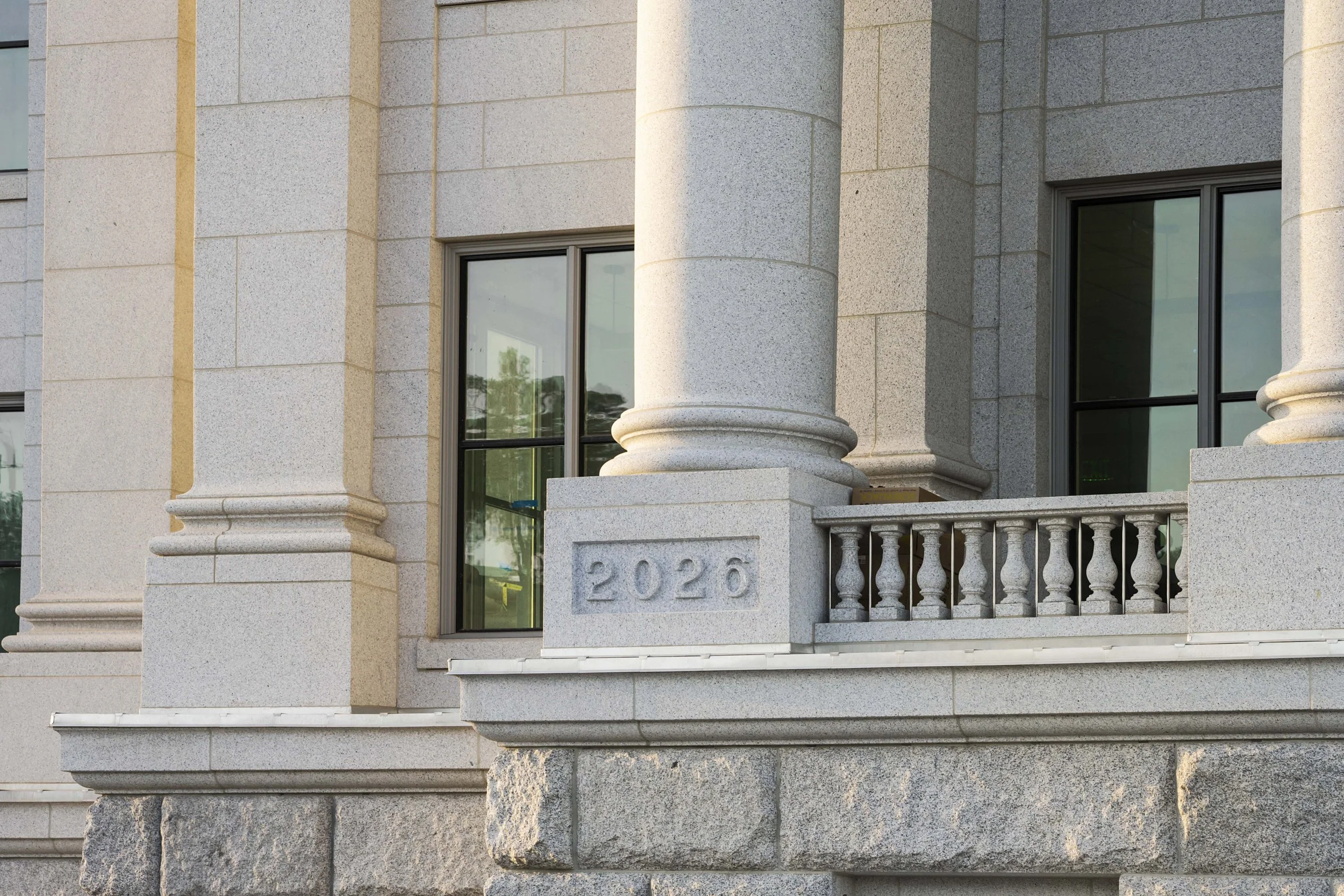 Close-up of a building's corner with large stone columns, windows, and a carved stone plaque with the year '2020' on it.