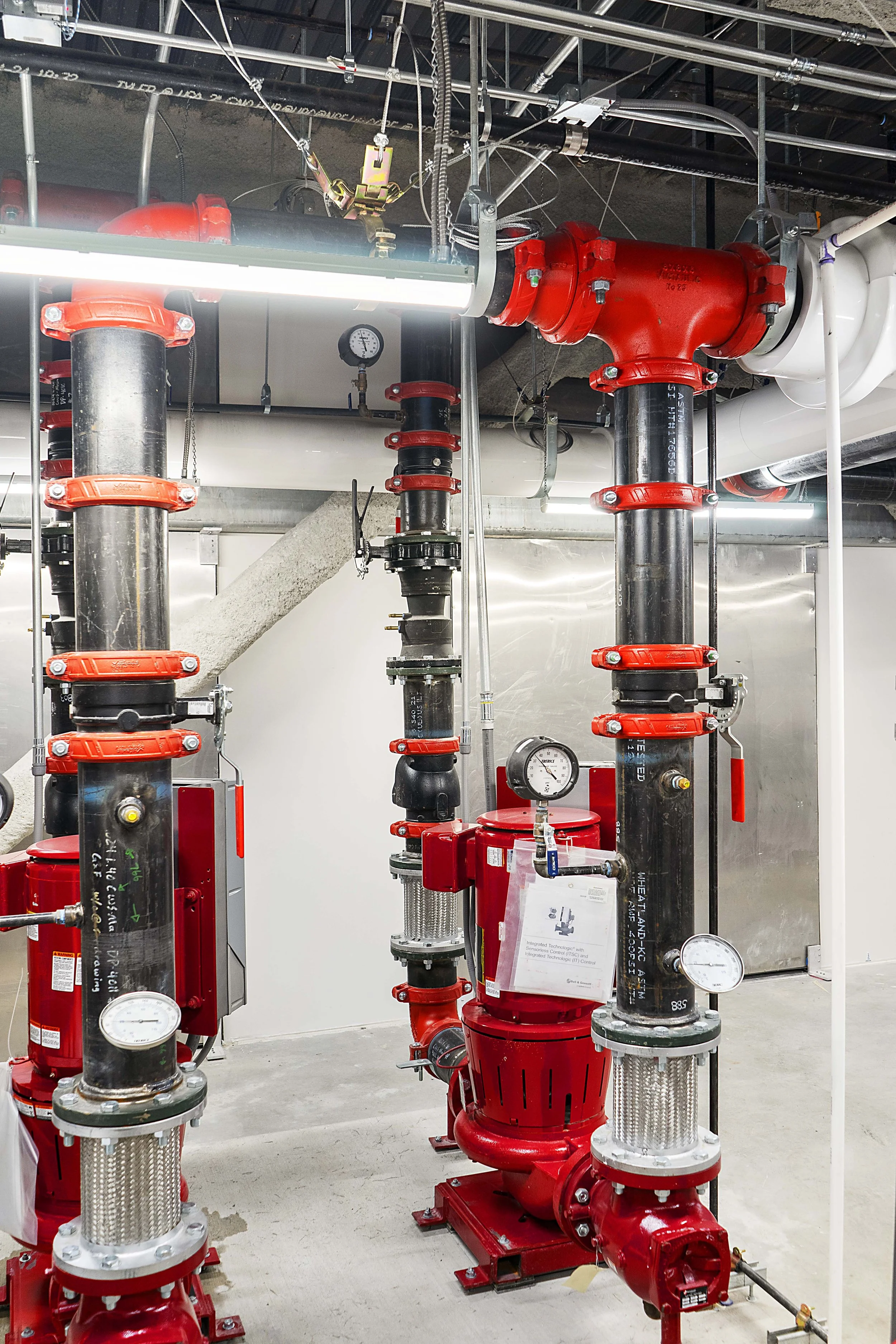 Fire protection sprinkler system with red pipes, valves, pressure gauges, and a pump installed in a mechanical room.