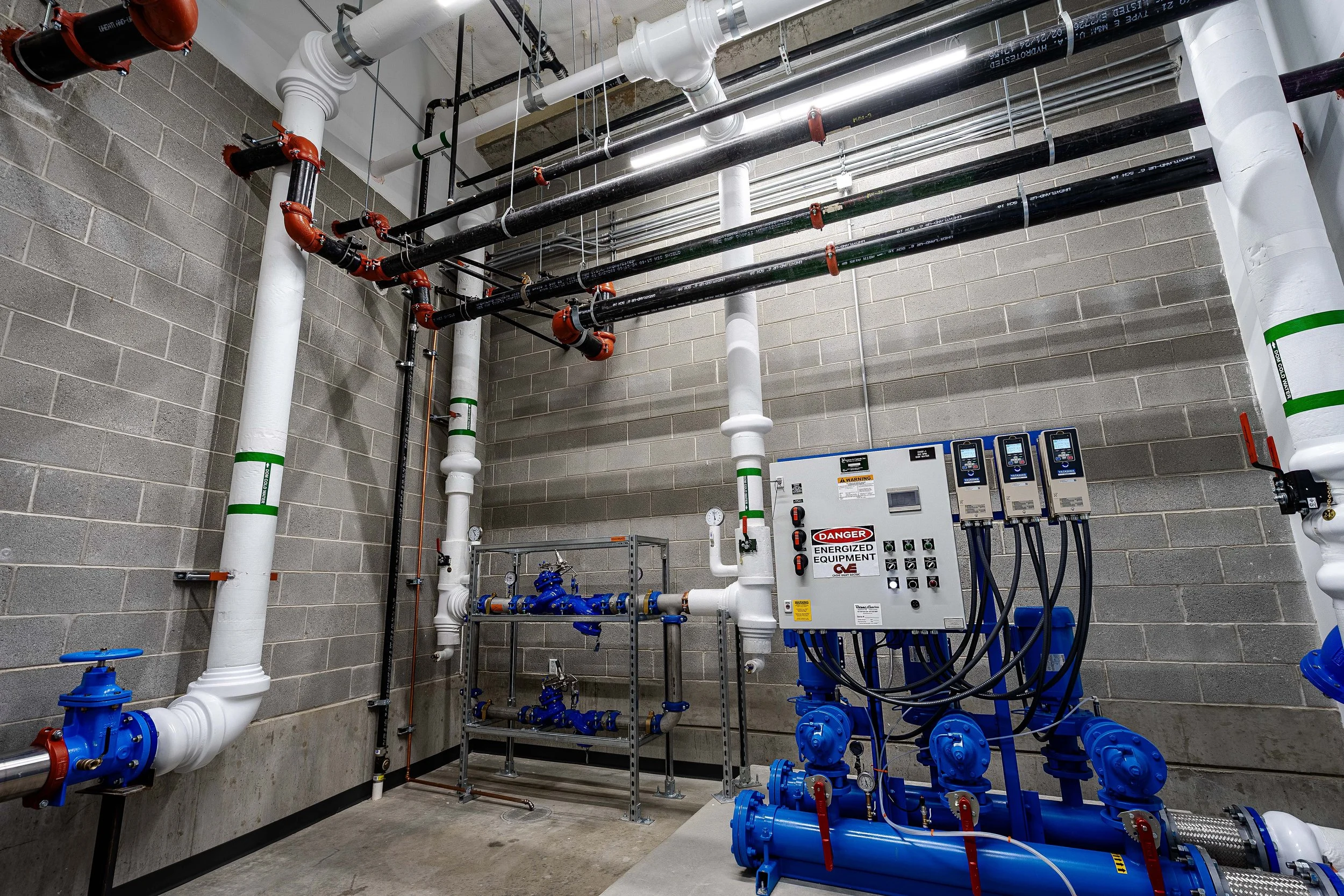 Industrial plumbing system with white and black pipes, blue valves, and control panels in a utility room.