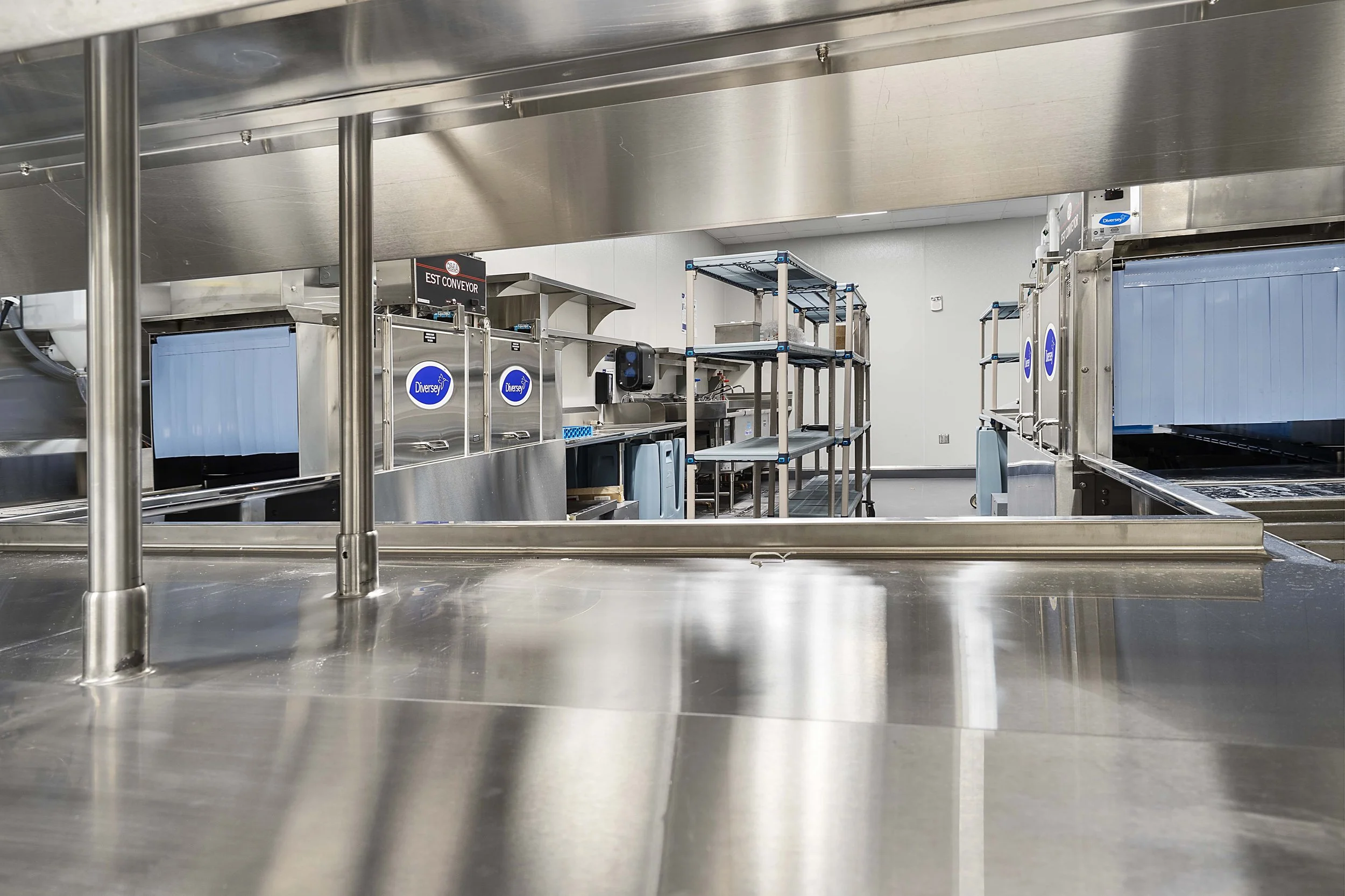 Empty industrial kitchen with stainless steel equipment, shelving, and conveyor belts.