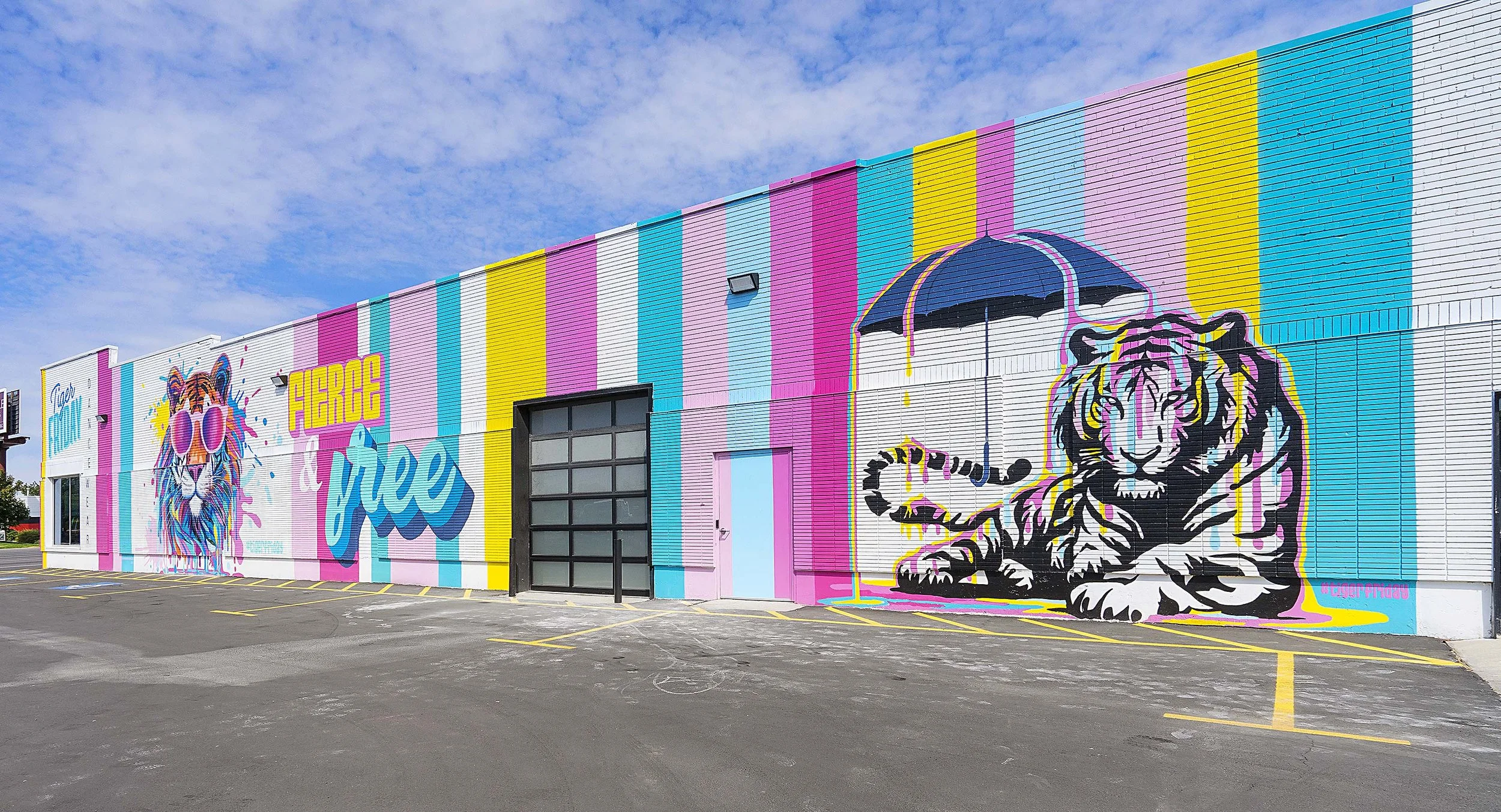 Colorful mural on building wall with a lion wearing sunglasses and a tiger holding an umbrella, surrounded by pink, yellow, blue, and white stripes.