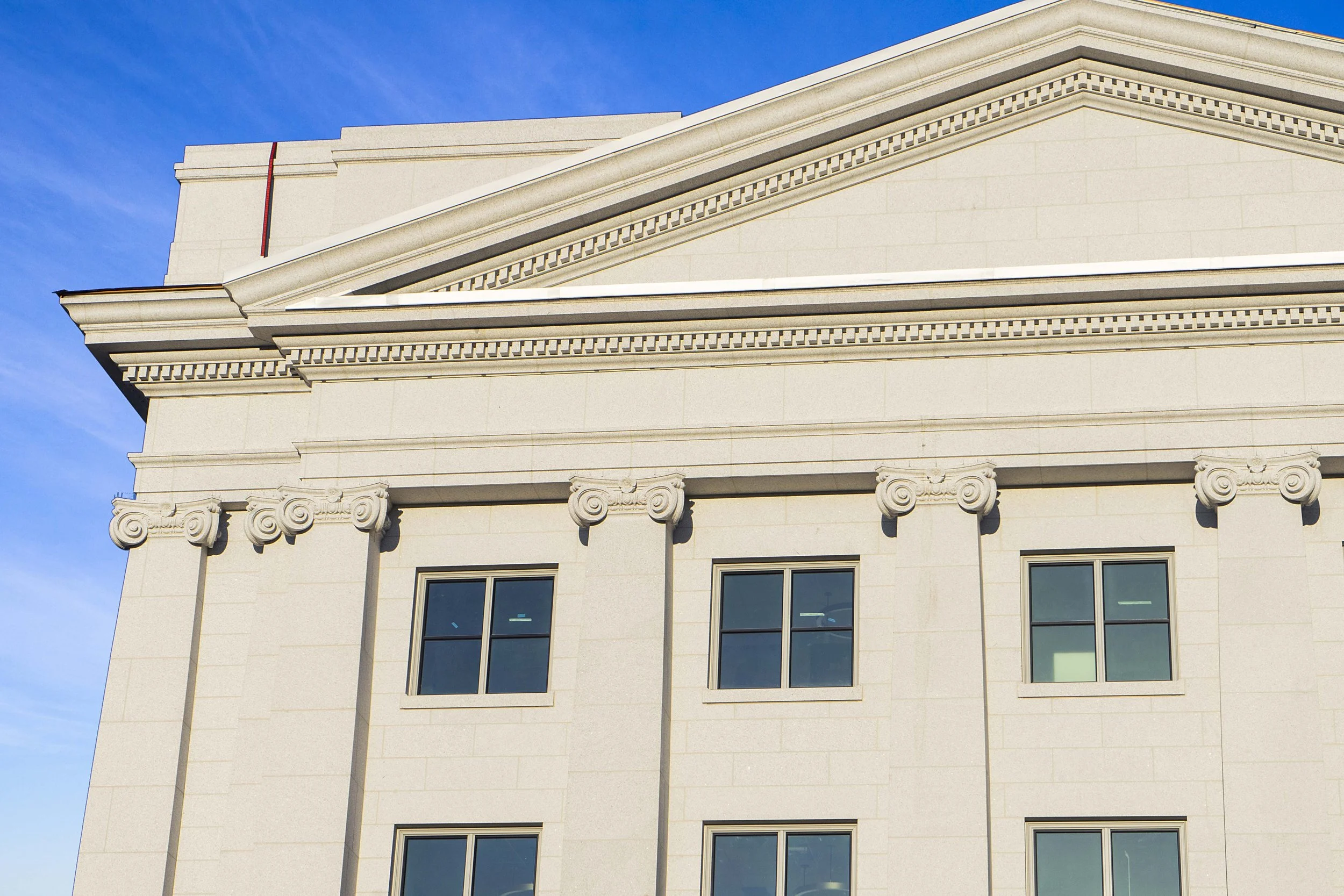 Close-up of the upper portion of a white classical-style building with decorative columns and friezes, set against a blue sky with some clouds.
