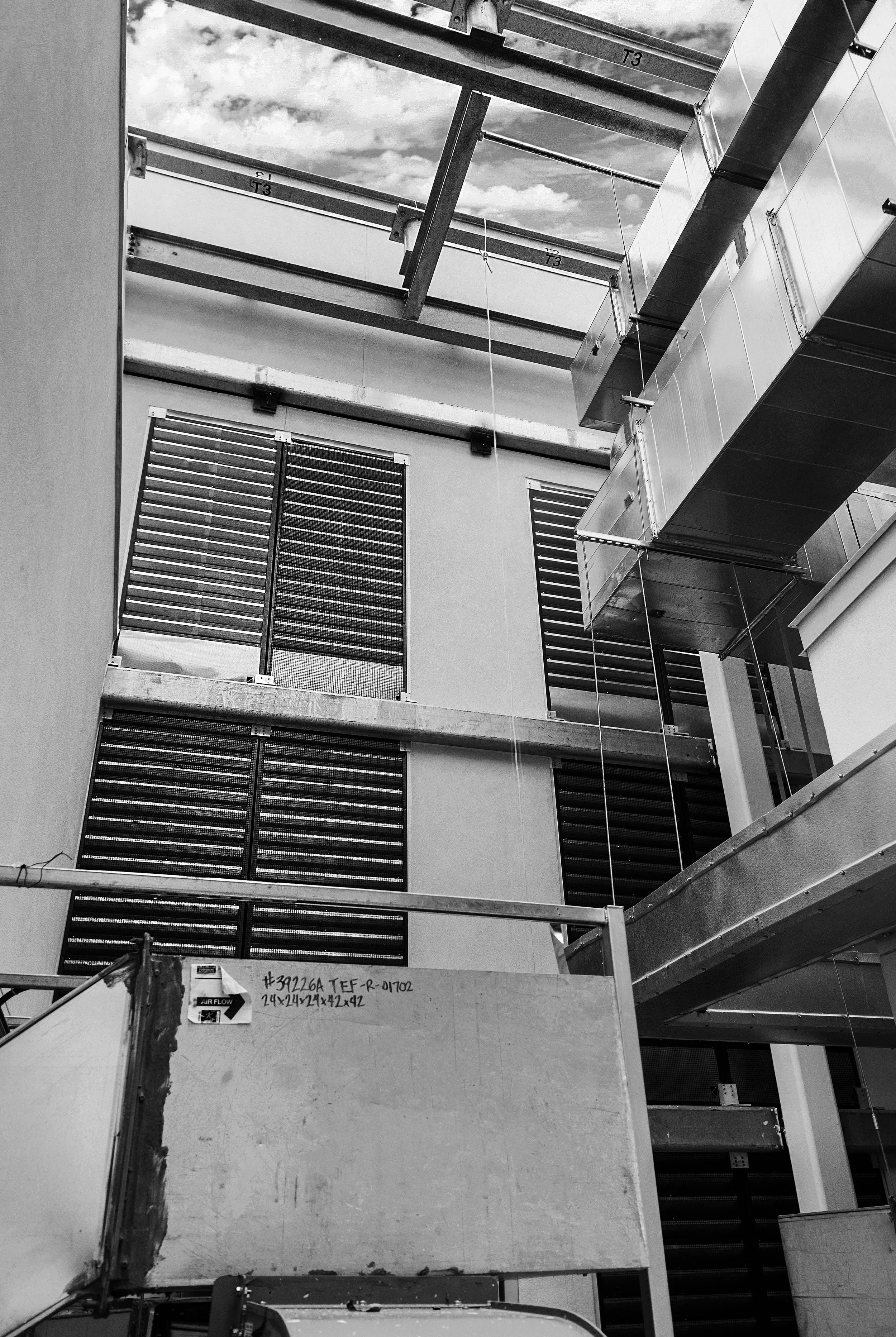 Construction site with metal framework, building walls, and ventilation ductwork, seen from below.
