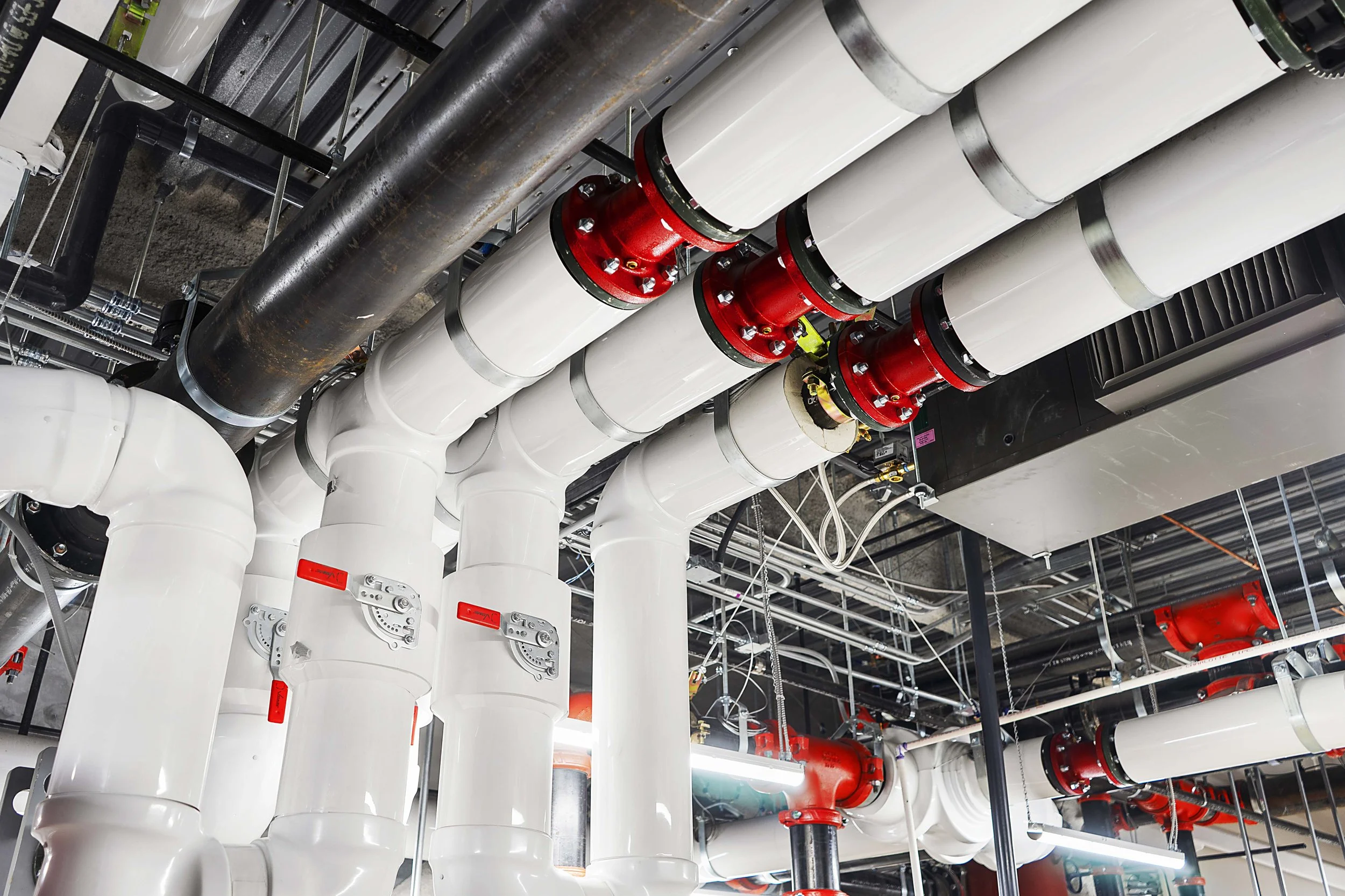 A complex network of white pipes and red valves in an industrial or commercial building plumbing system.