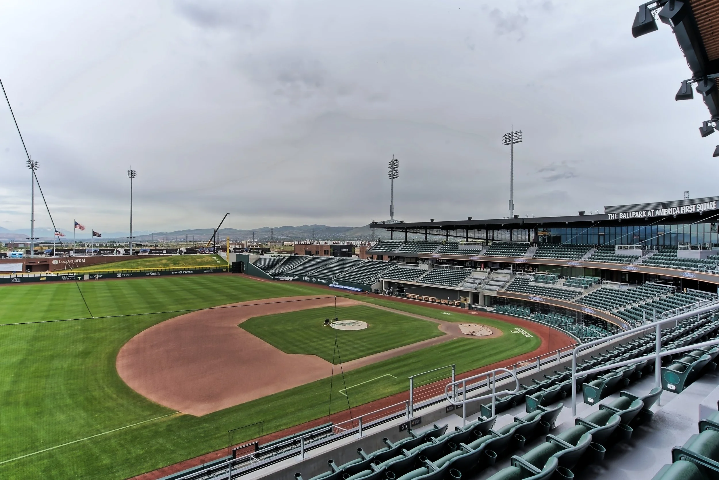 Empty baseball stadium with green grass and brown dirt on the field, empty seats, and an overcast sky.
