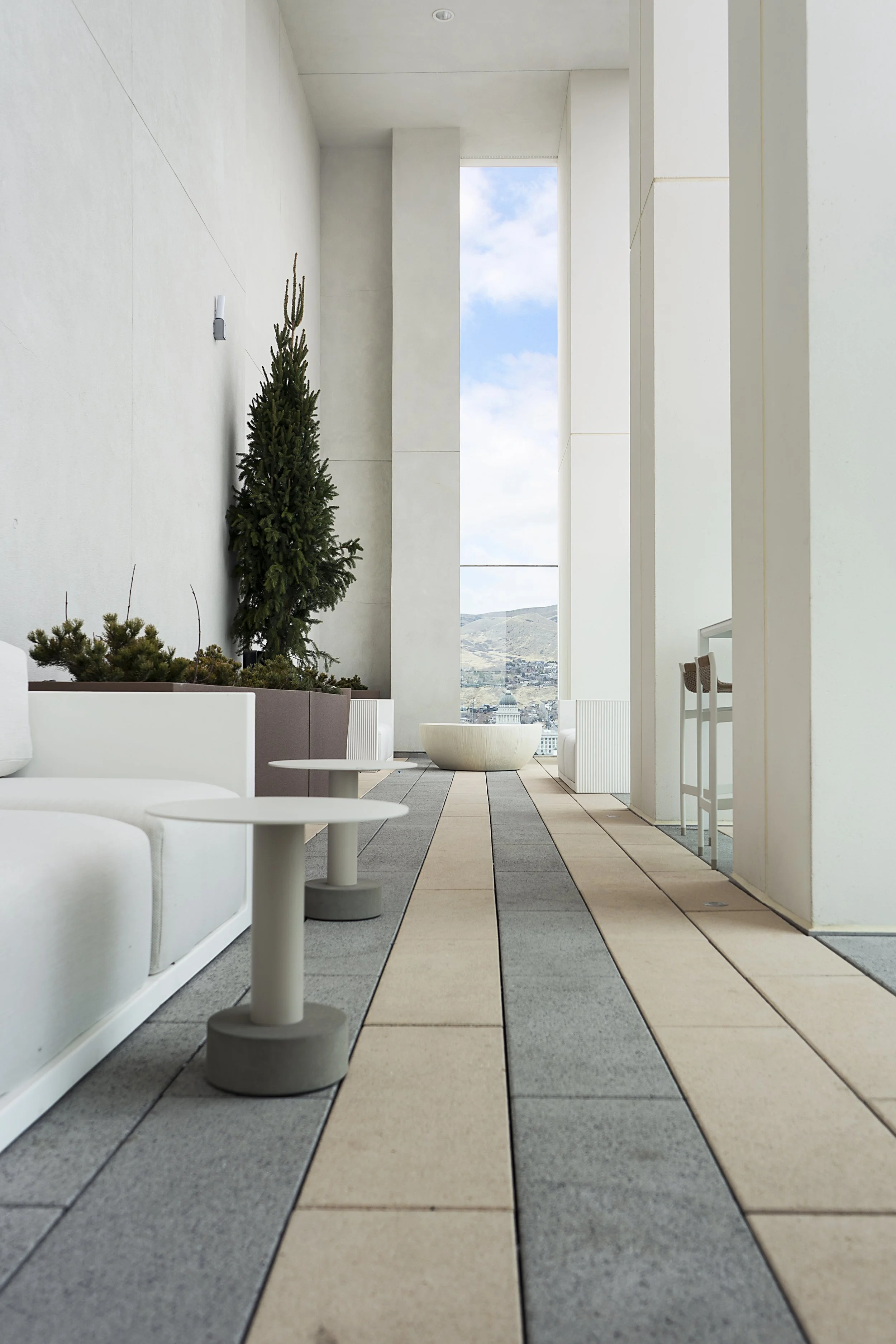 Modern balcony with white furniture, a small tree, and a view of hills and sky.