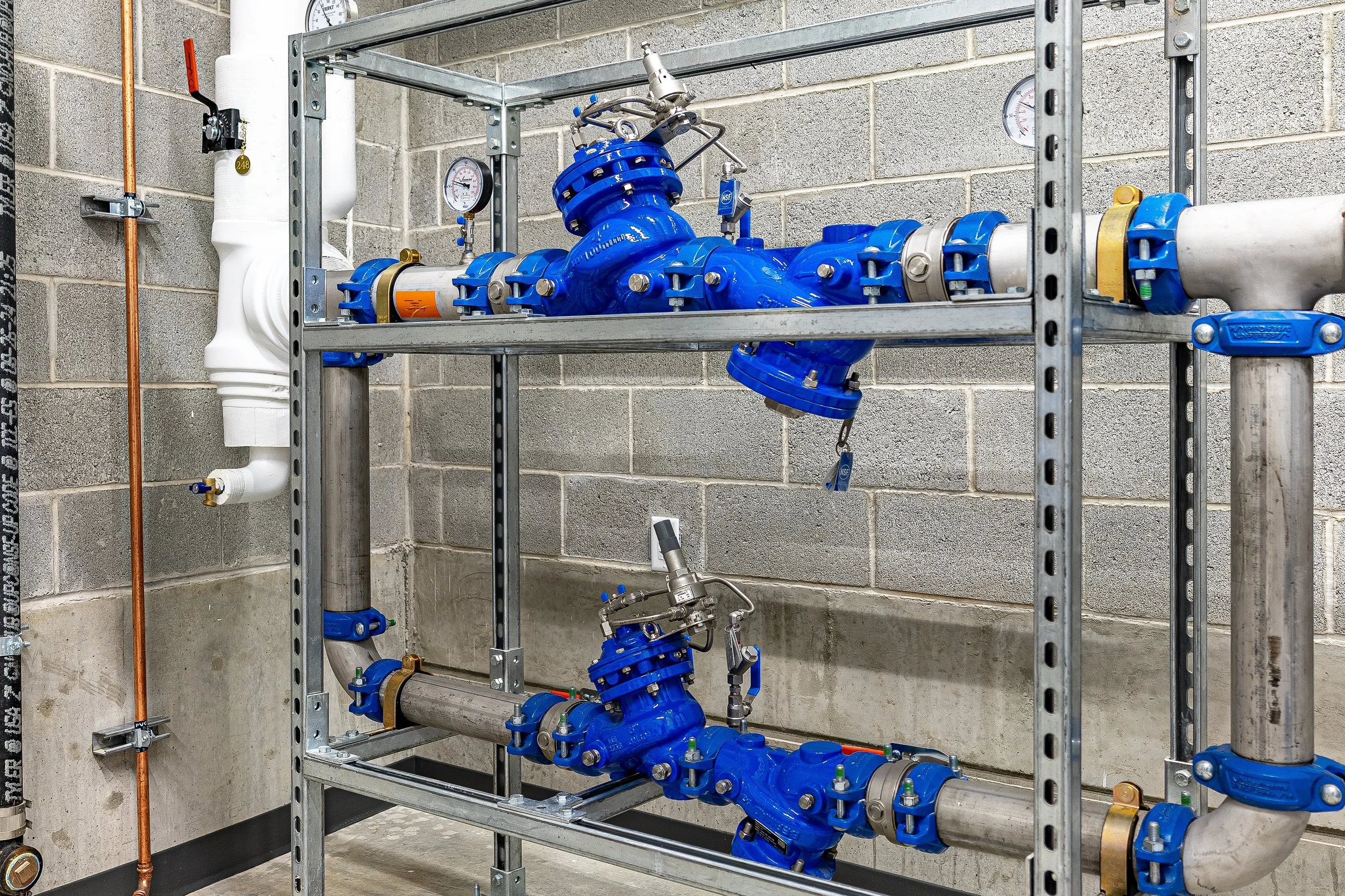 Blue industrial valves and pipes mounted on a metal frame against a concrete wall in a mechanical room.