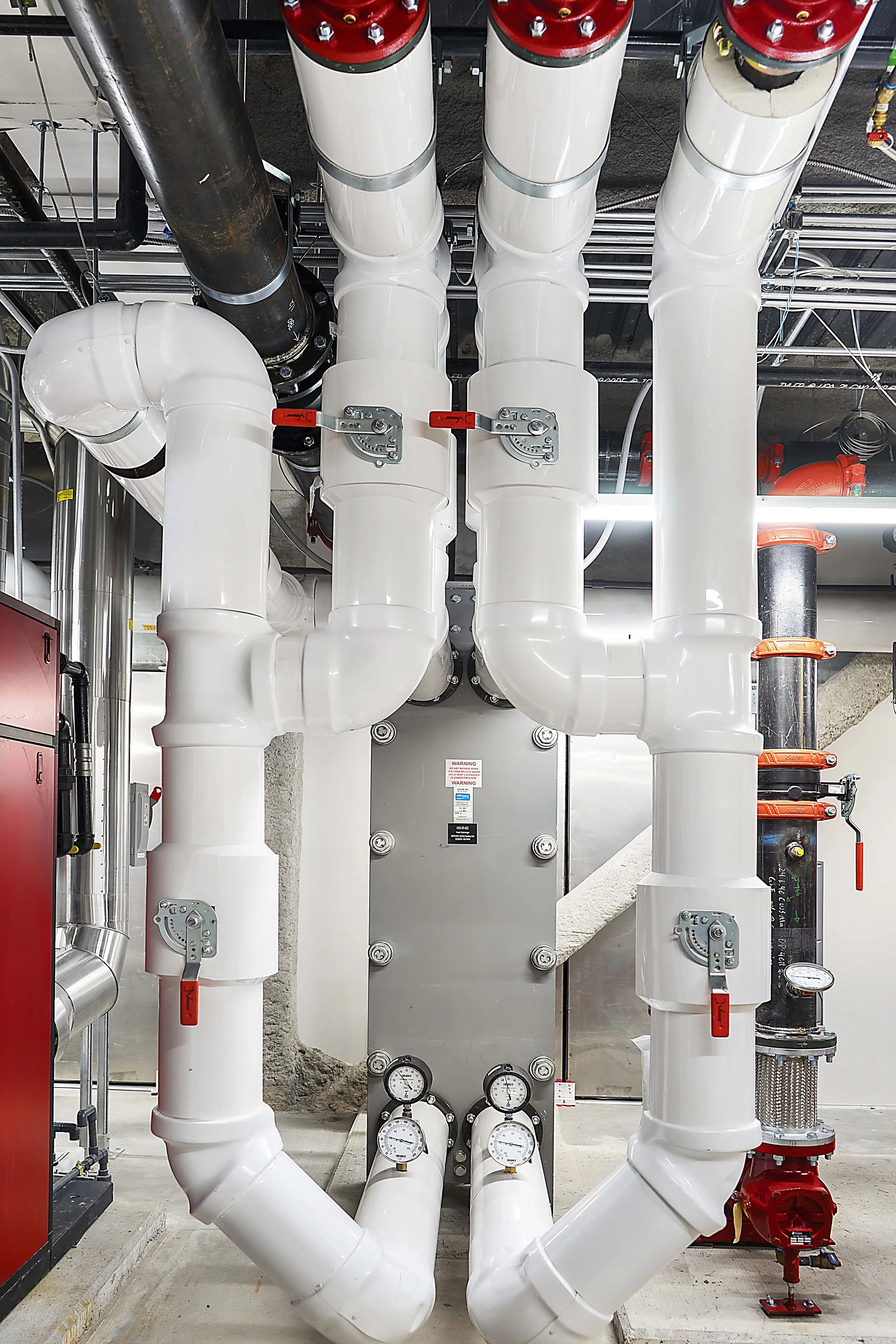 Industrial piping system with white pipes, red valves, and gauges.