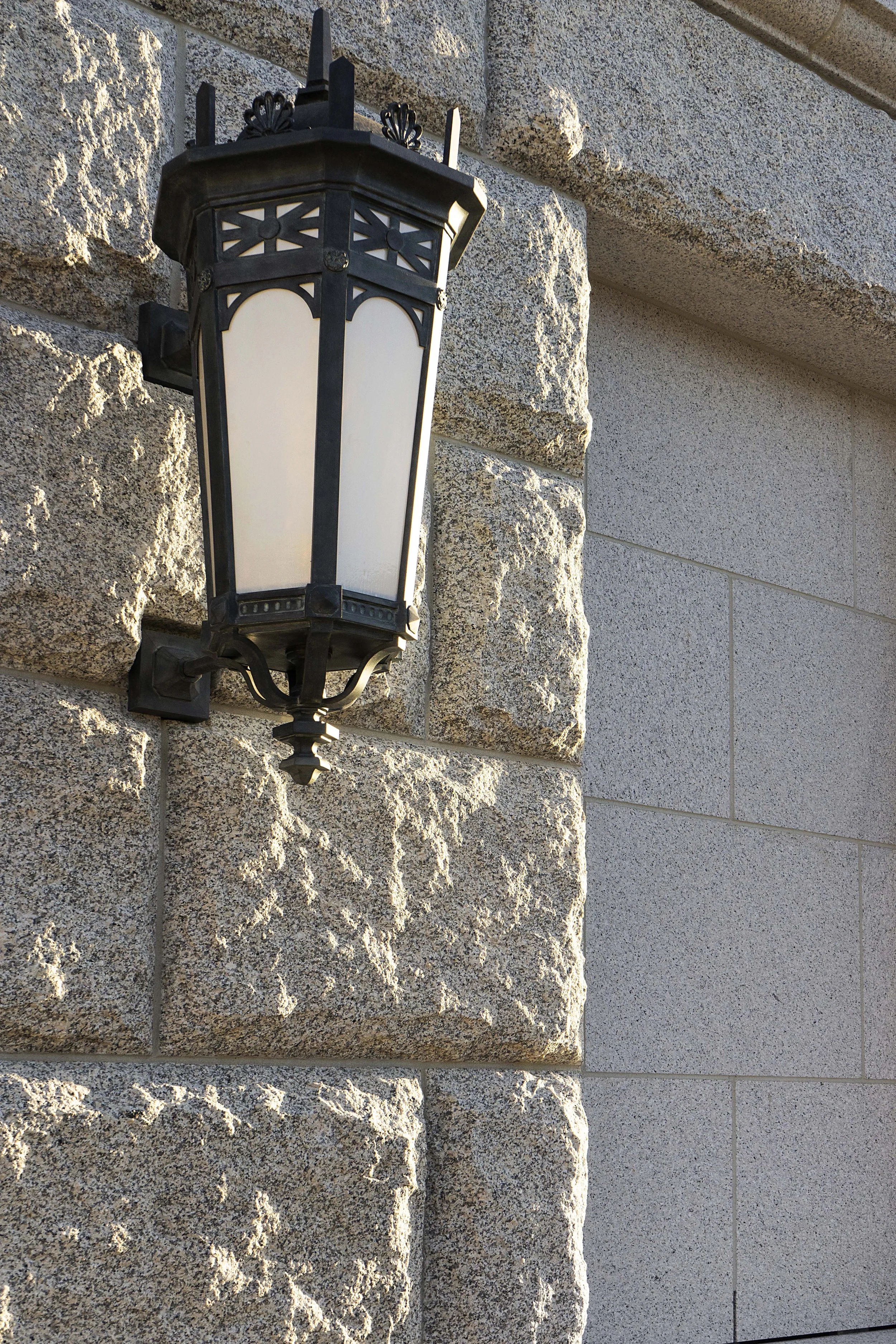 A decorative outdoor lantern mounted on a stone wall of a building.