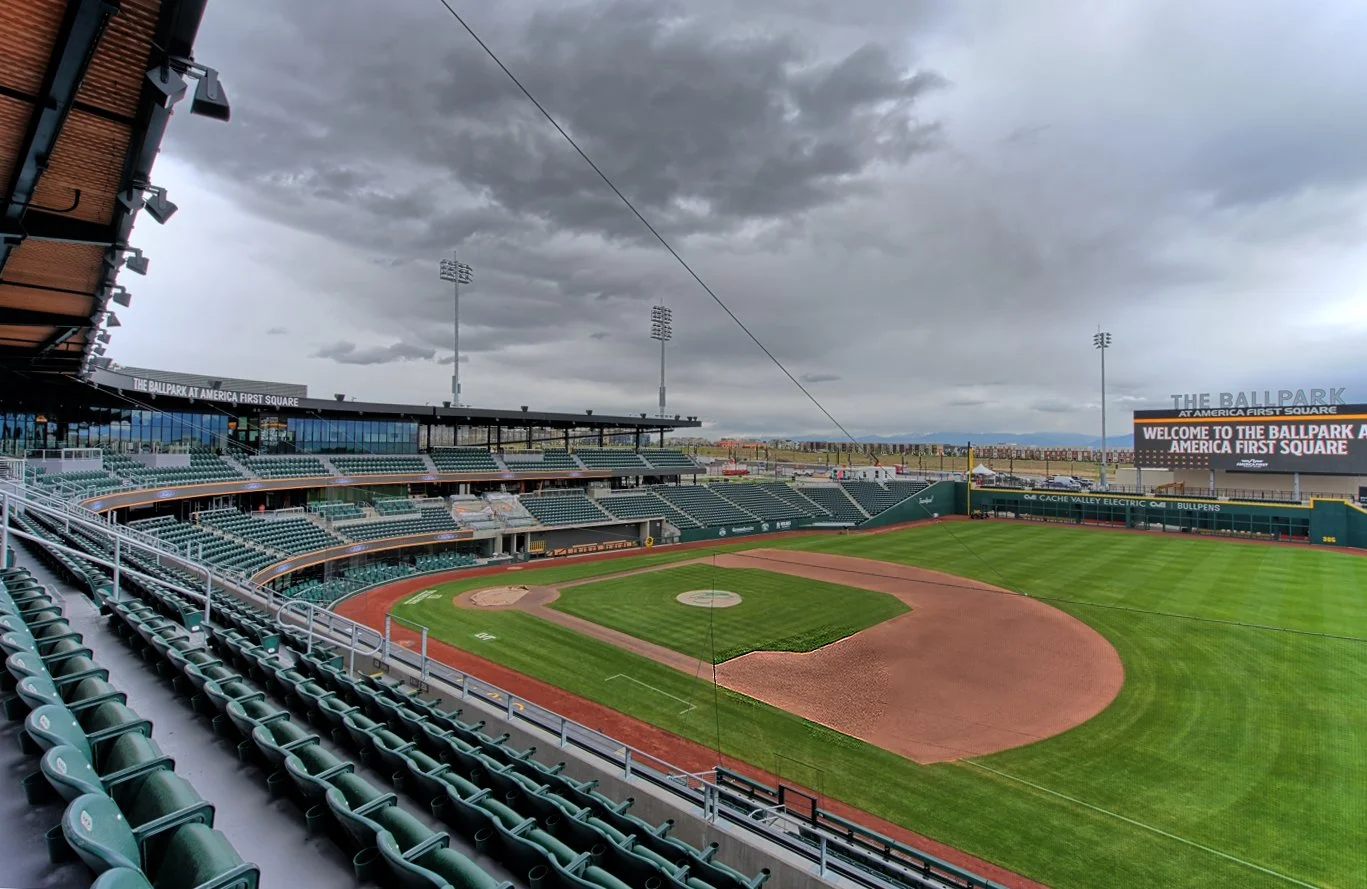 Empty baseball stadium with green field and cloudy sky, digital scoreboard displaying welcome message at America First Square.