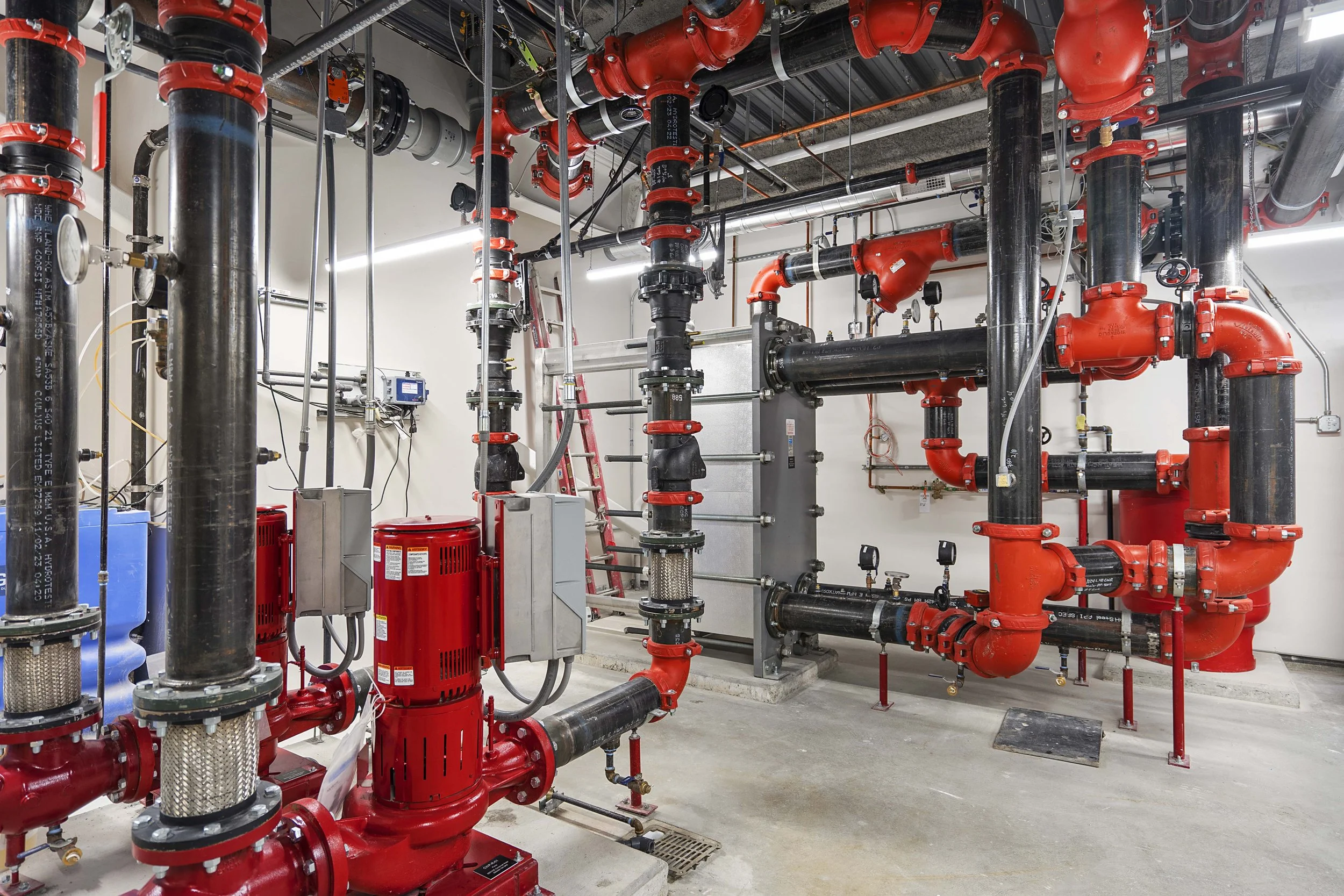 Industrial piping system with black and red pipes, valves, and gauges in a utility room.