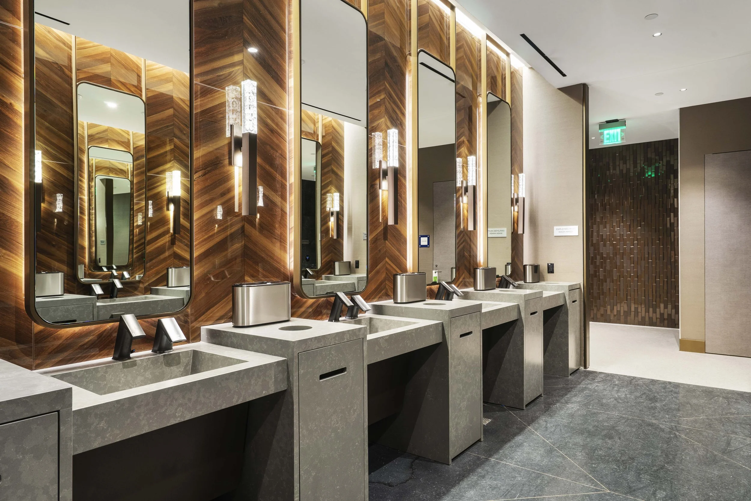 Public restroom with multiple sinks, mirrors, and wall-mounted light fixtures in a modern, upscale design.