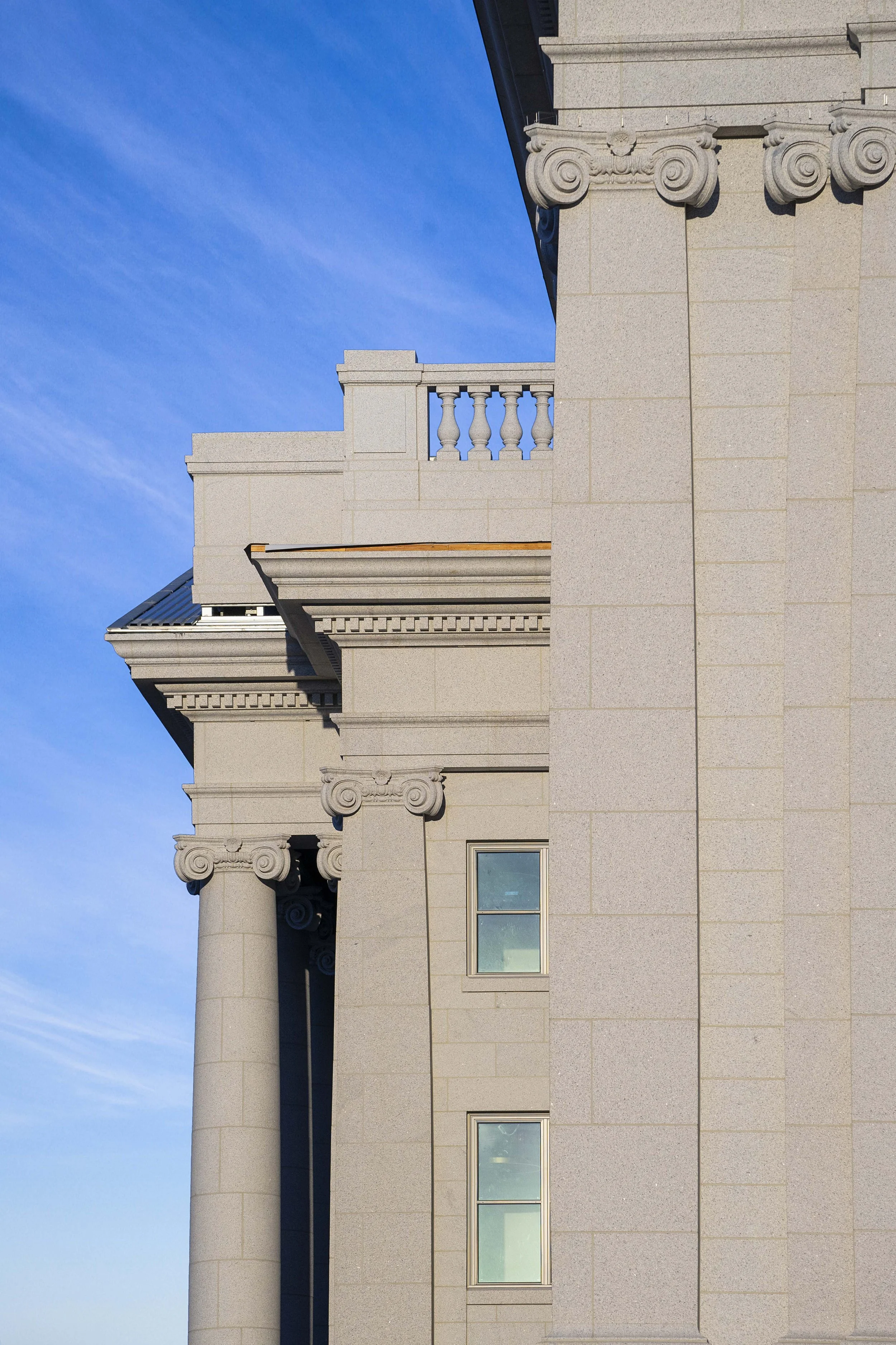Close-up of a classical building with columns, a balcony, decorative capitals, and windows under a blue sky.